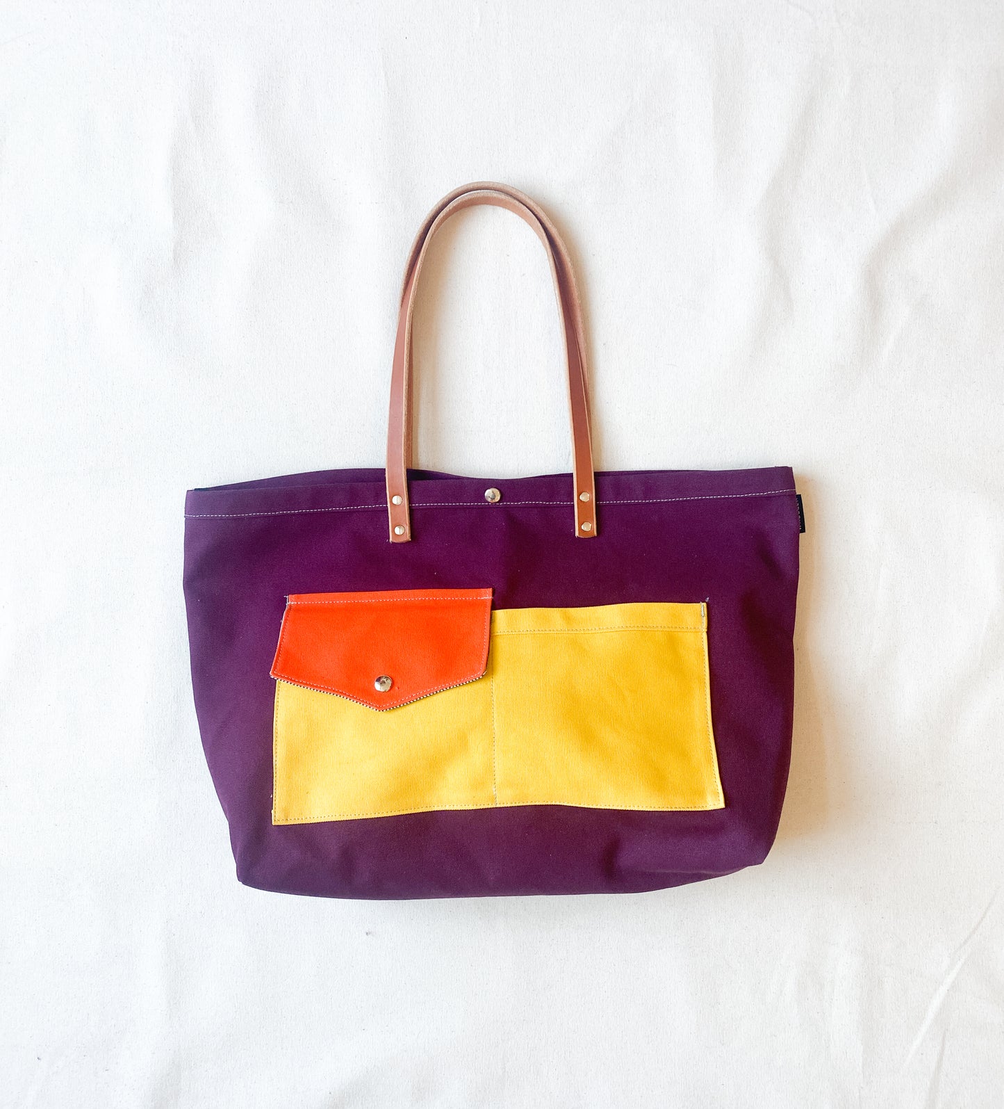Multi-color (yellow, purple, orange) canvas beach tote with leather straps.