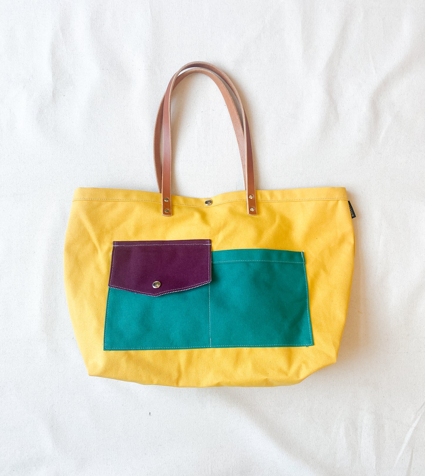 Multi-color (yellow, purple, teal) canvas beach tote with leather straps.