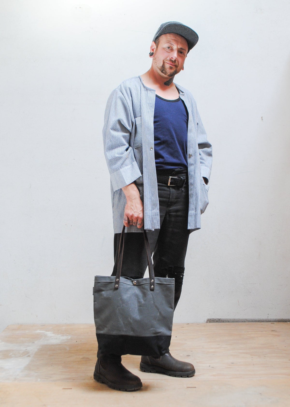 Queer person holding a gray tote bag against a plain background