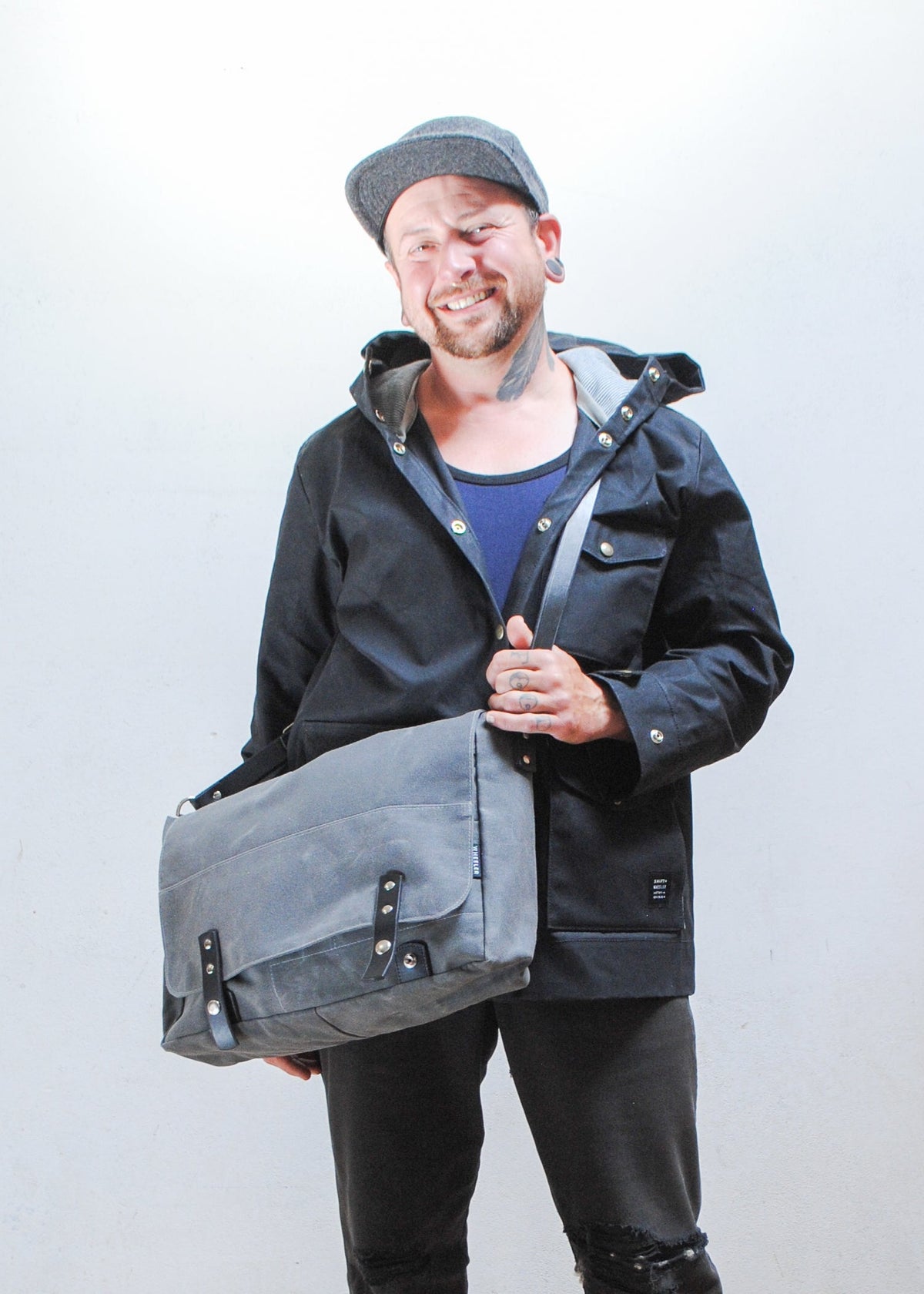 Model wearing black Shift + Wheeler black raincoat and charcoal Shift + Wheeler waxed canvas messenger bag over the back of shoulder