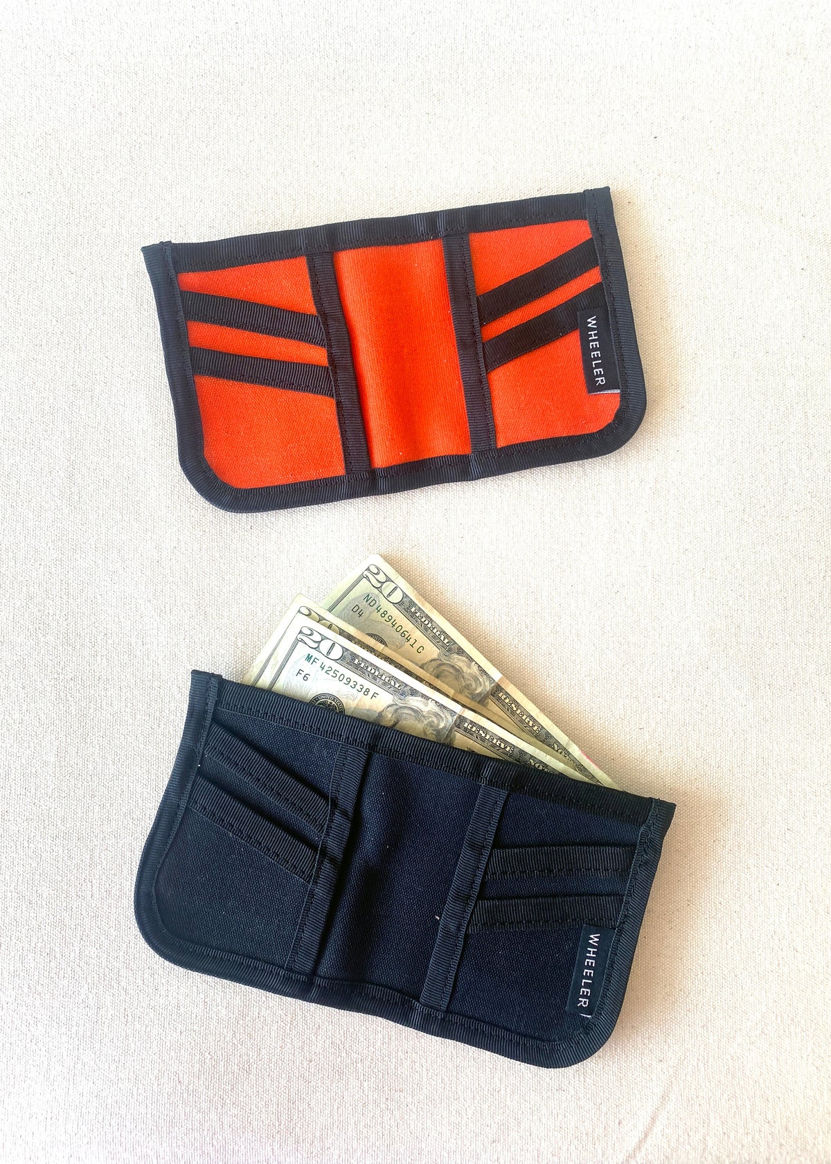 2 waxed canvas wallets (orange and black option) laid flat on table, view of inside of wallets with cash peaking out of one wallet