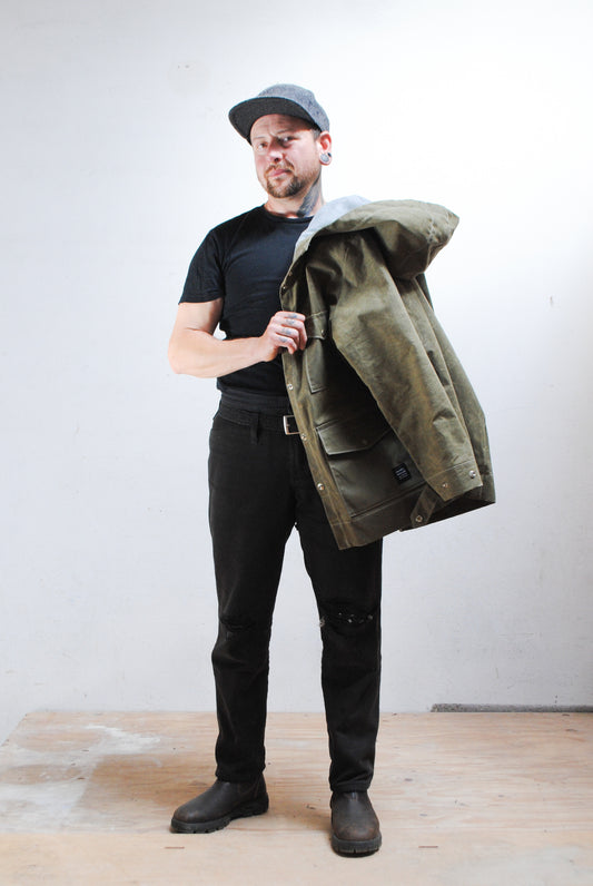 Man wearing a green jacket over a black shirt with a plain background