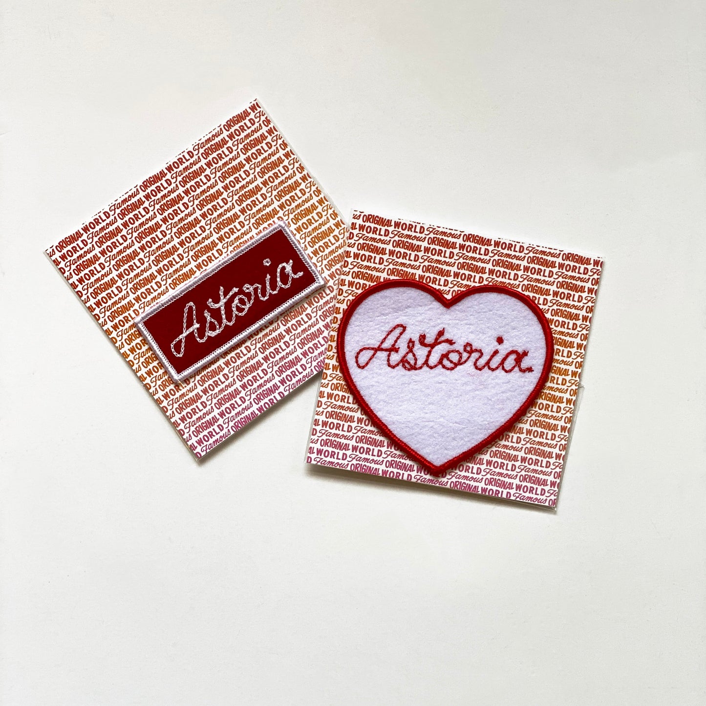Handmade, custom "Astoria" heart in white felt with red embroidery and "Astoria" rectangle red felt patch with white embroidery, mounted on World Famous Original packaging.
