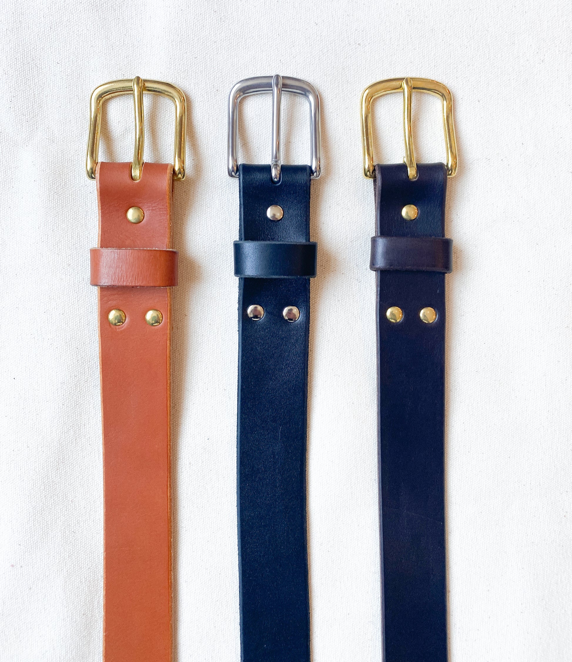 Leather belt in tan with brass, black with silver, and dark brown and brass.