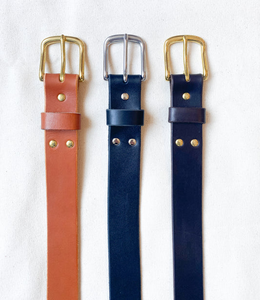 Leather belt in tan with brass, black with silver, and dark brown and brass.