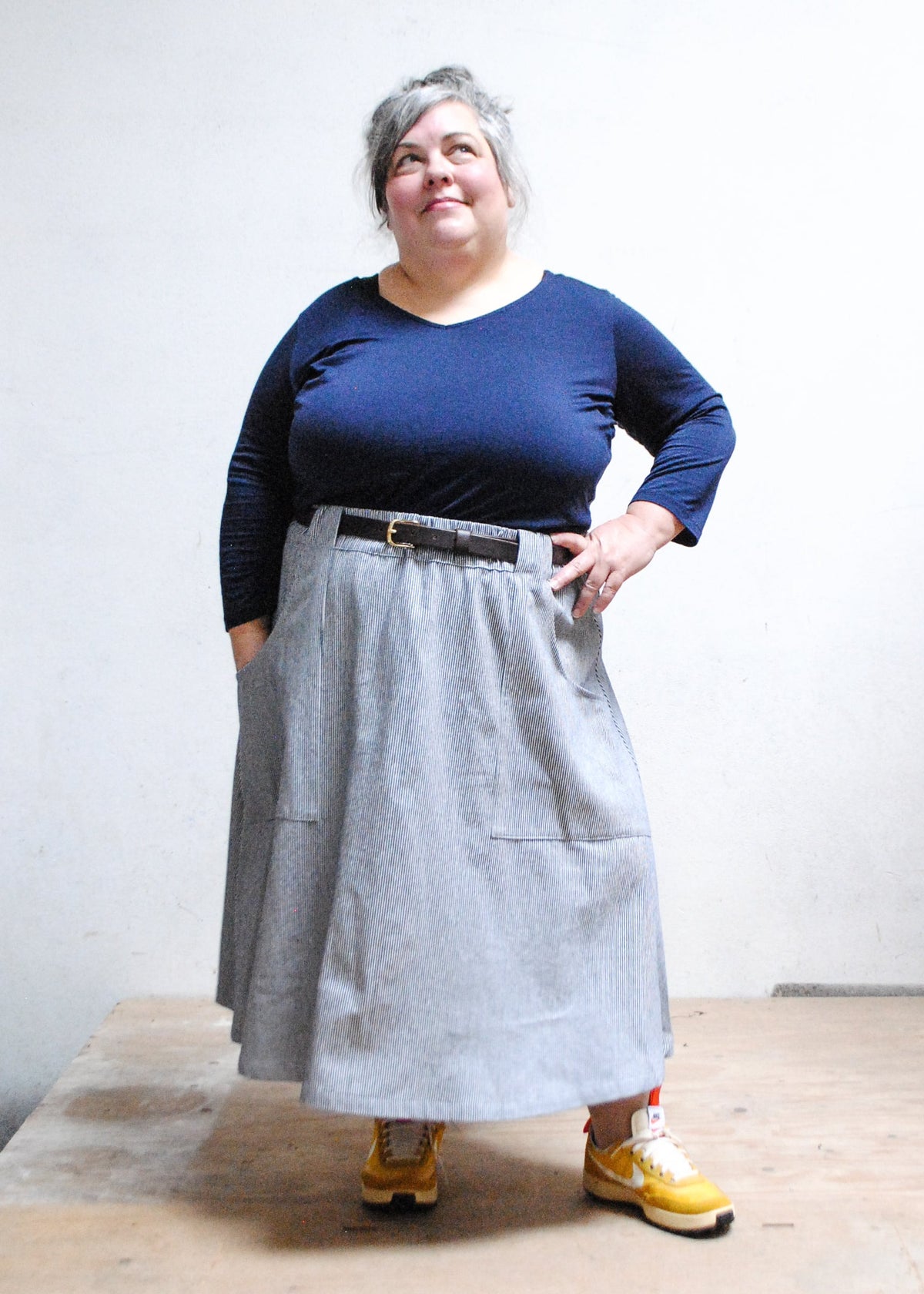 Model in blue long sleeve top, tennis shoes, and Shift + Wheeler handmade railroad stripe skirt, one hand on hip