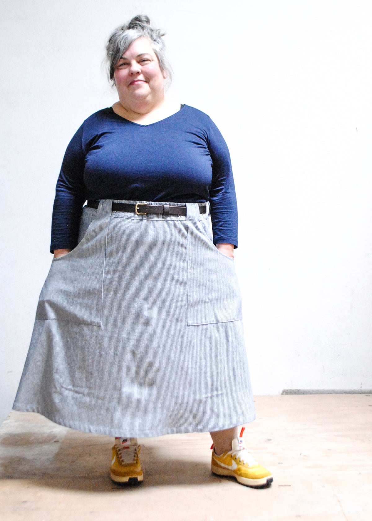 Model in blue long sleeve shirt, railroad strip vest, yellow sneakers, and Shift + Wheeler handmade railroad stripe skirt - hands in skirt pockets