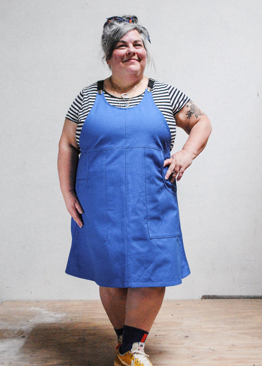 Model wearing Shift + Wheeler blue suspender dress over a black and white striped t-shirt.