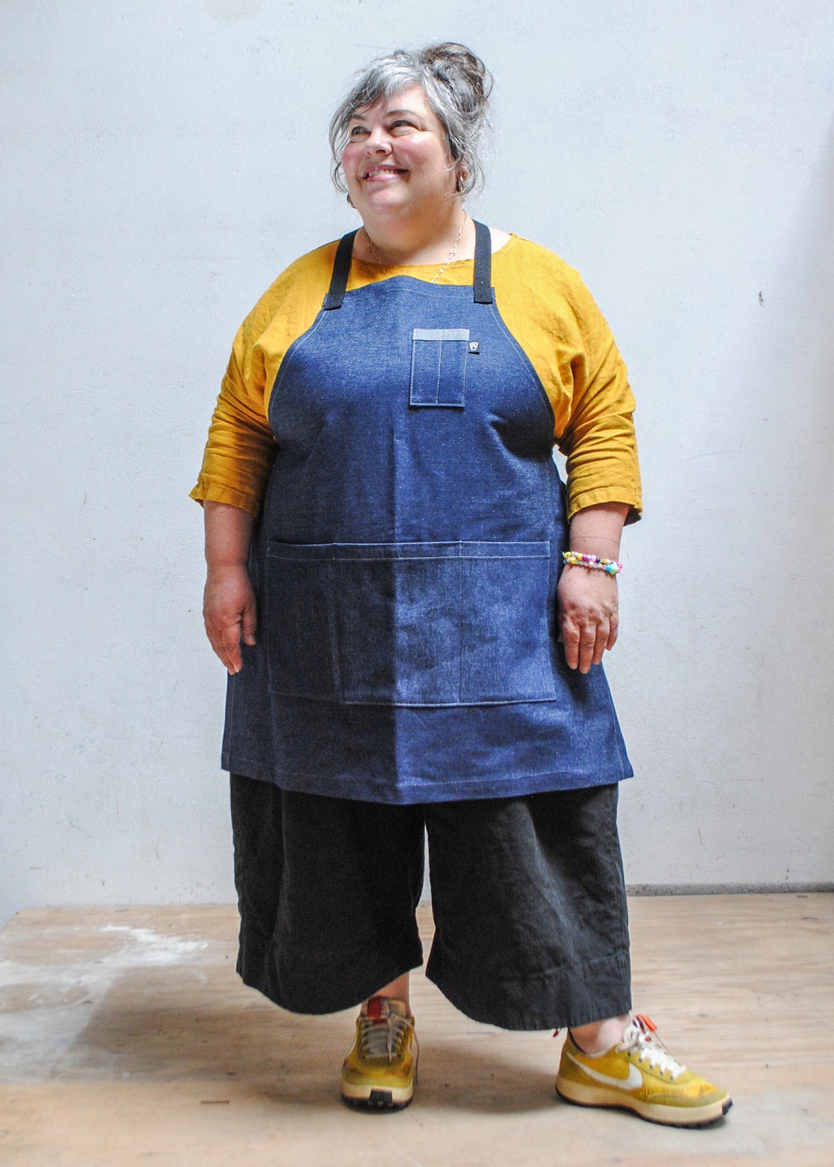 Model wearing yellow shirt, black pants, and Shift + Wheeler crossback denim apron