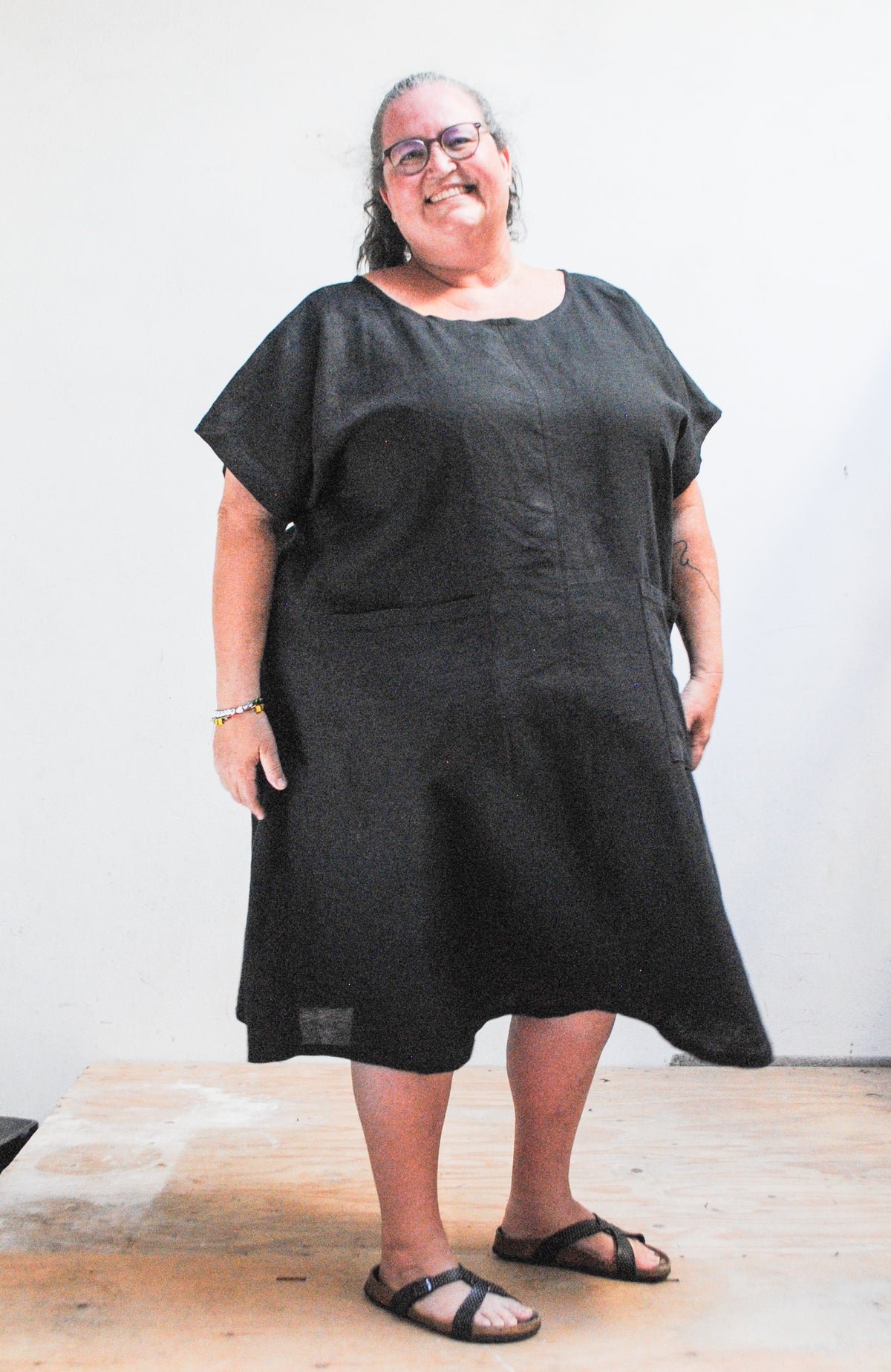 Person wearing a black dress standing against a white wall.
