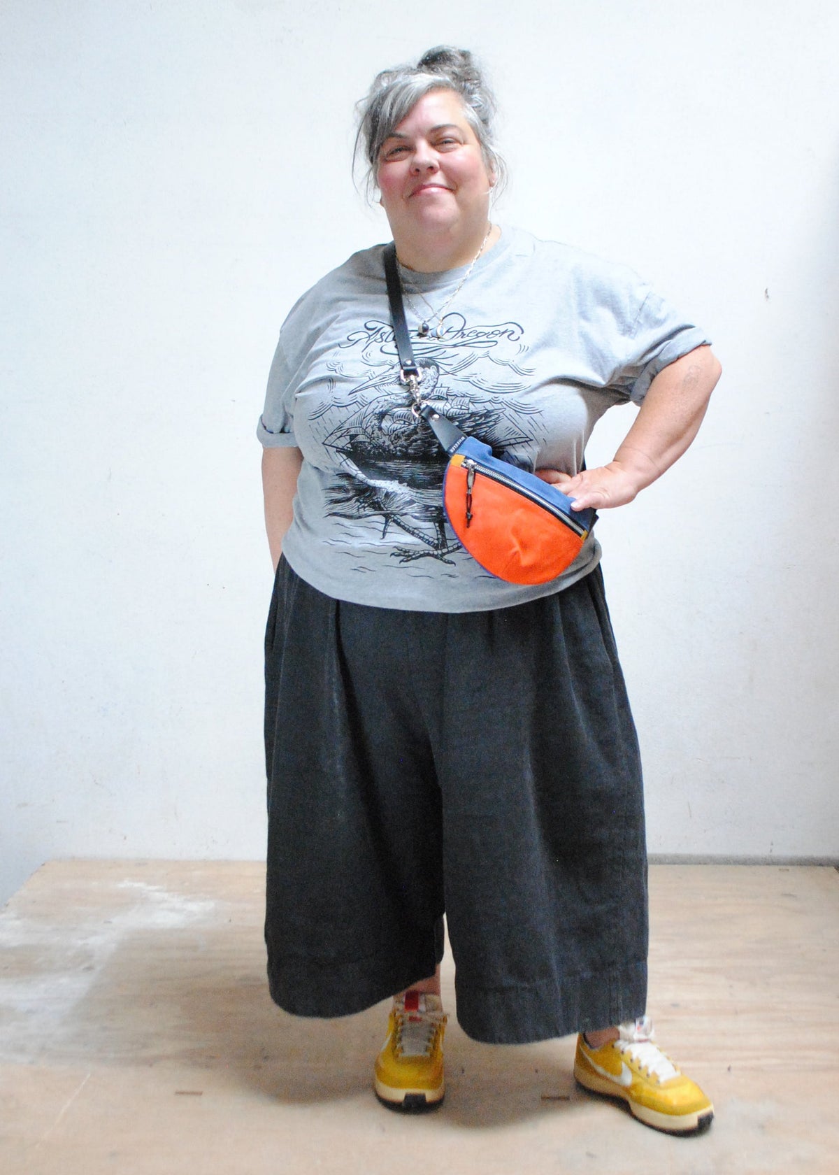 Model wearing handmade two-tone (orange and royal blue) color waxed canvas fanny pack, fanny pack is being worn over the shoulder and hand is on hip