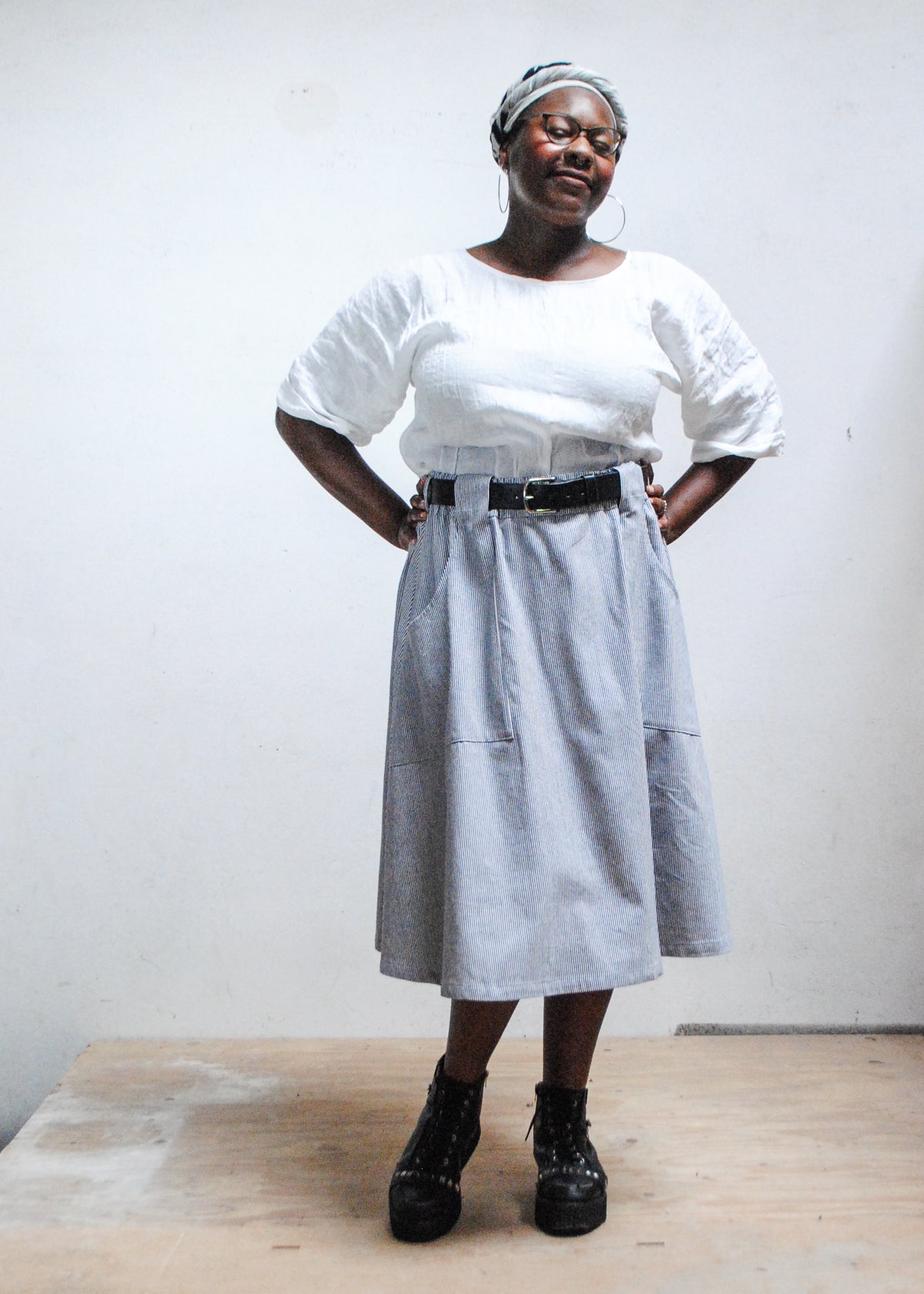 Model in white top, black boots, and Shift + Wheeler handmade railroad stripe skirt, hands on hips