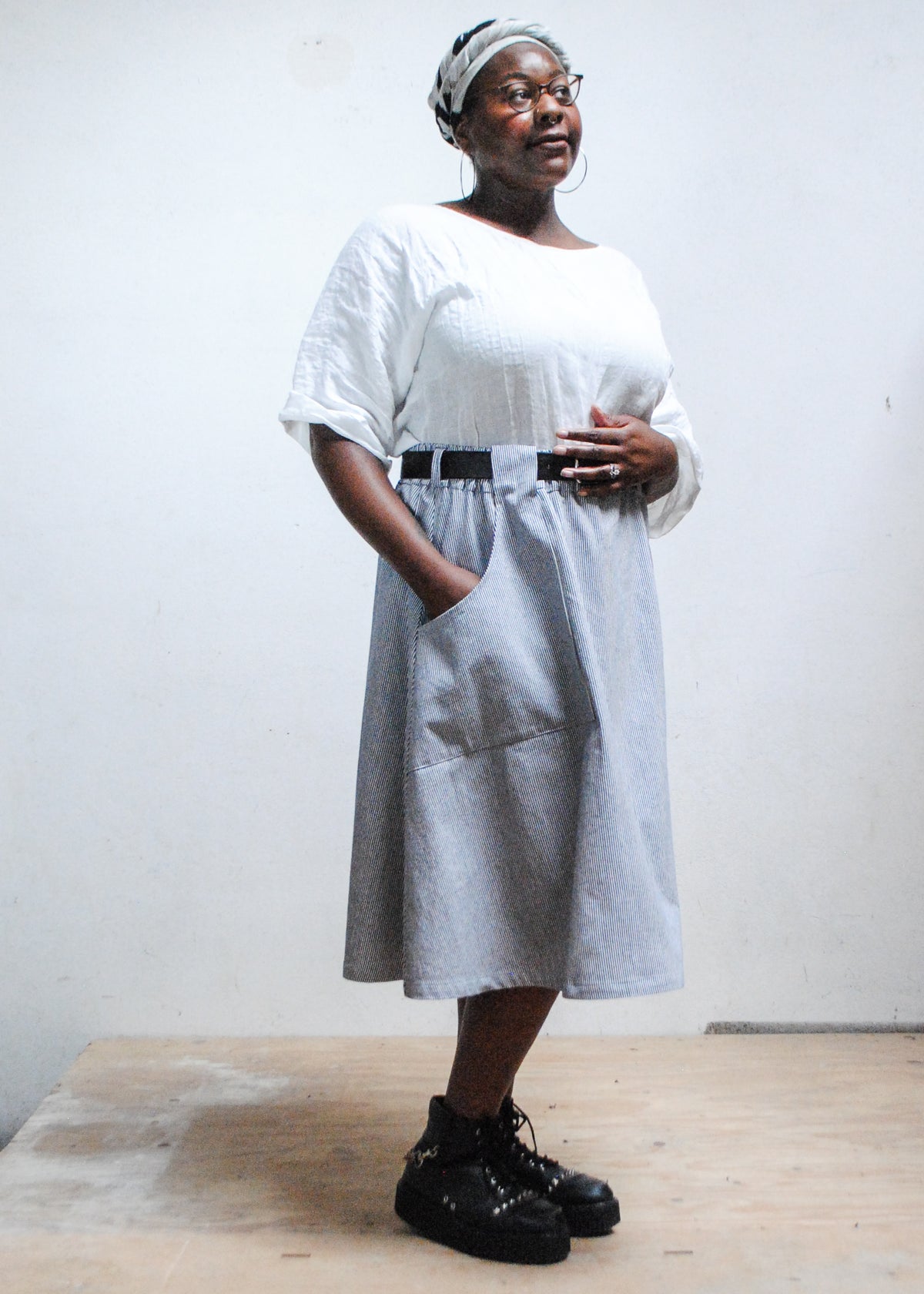 Model in white top, black boots, and Shift + Wheeler handmade railroad stripe skirt, one hand in skirt pocket