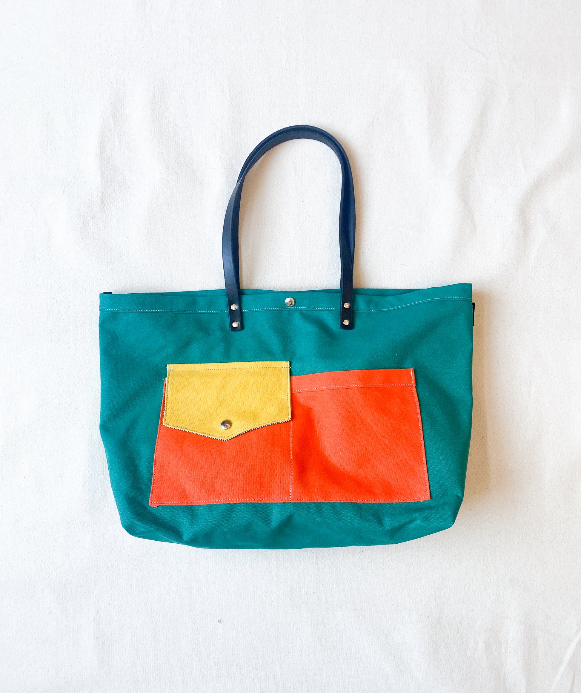 Multi-color (yellow, orange, teal) canvas beach tote with leather straps. 