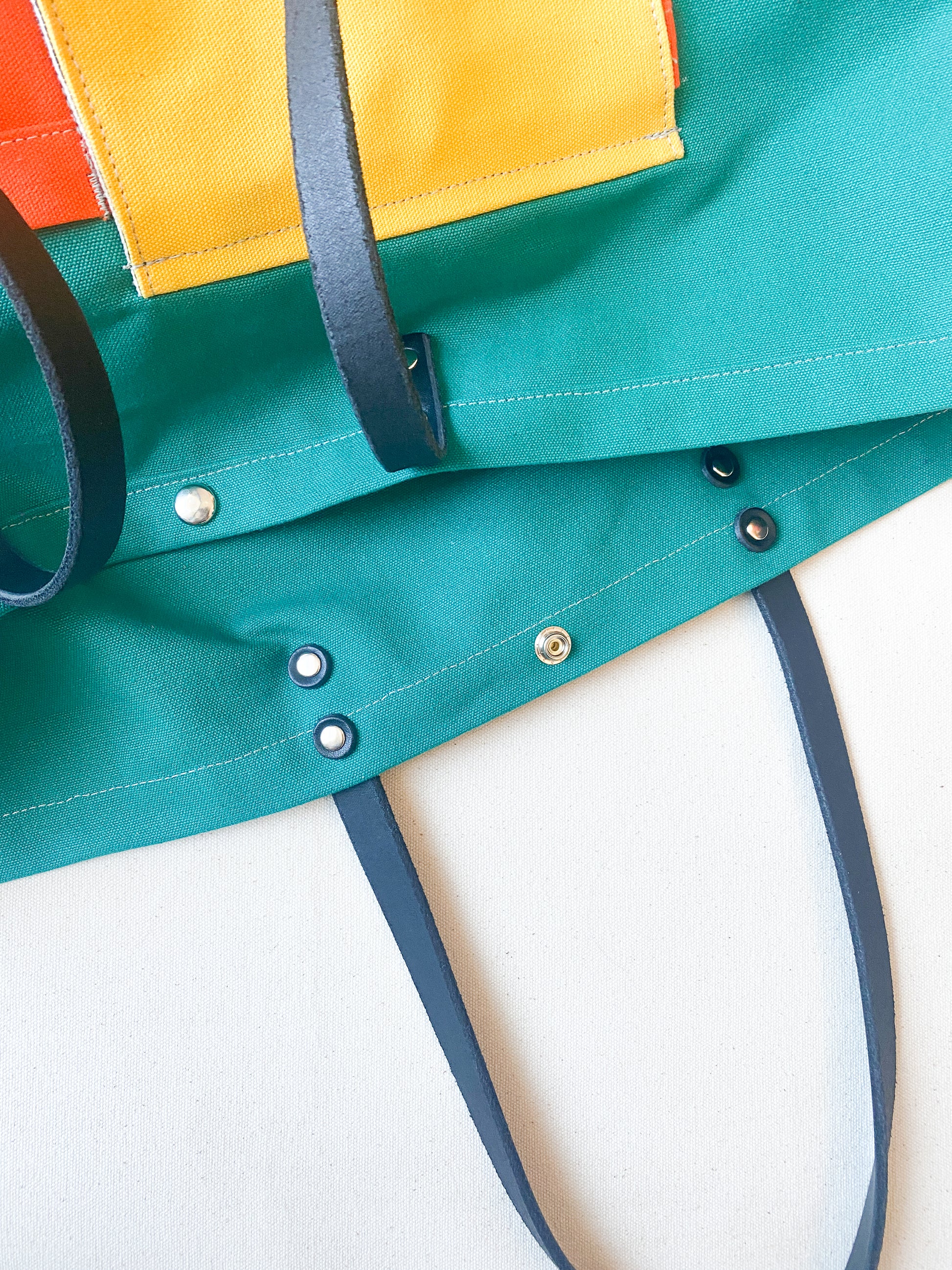 Multi-color (yellow, orange, teal) canvas beach tote with leather straps. Detail of the straps. 
