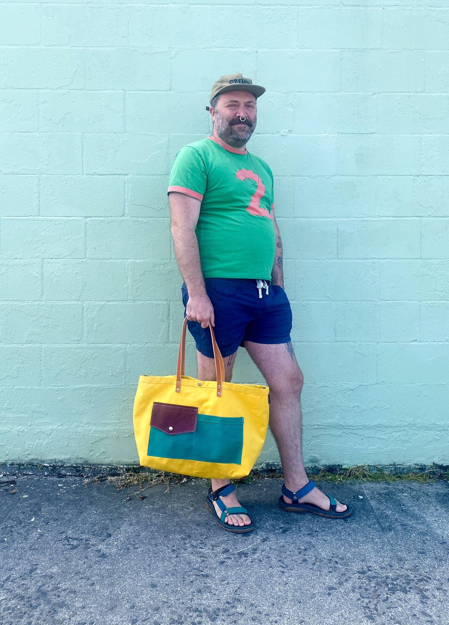 Multi-color (yellow, purple, teal) canvas beach tote with leather straps. Model is at an angle.