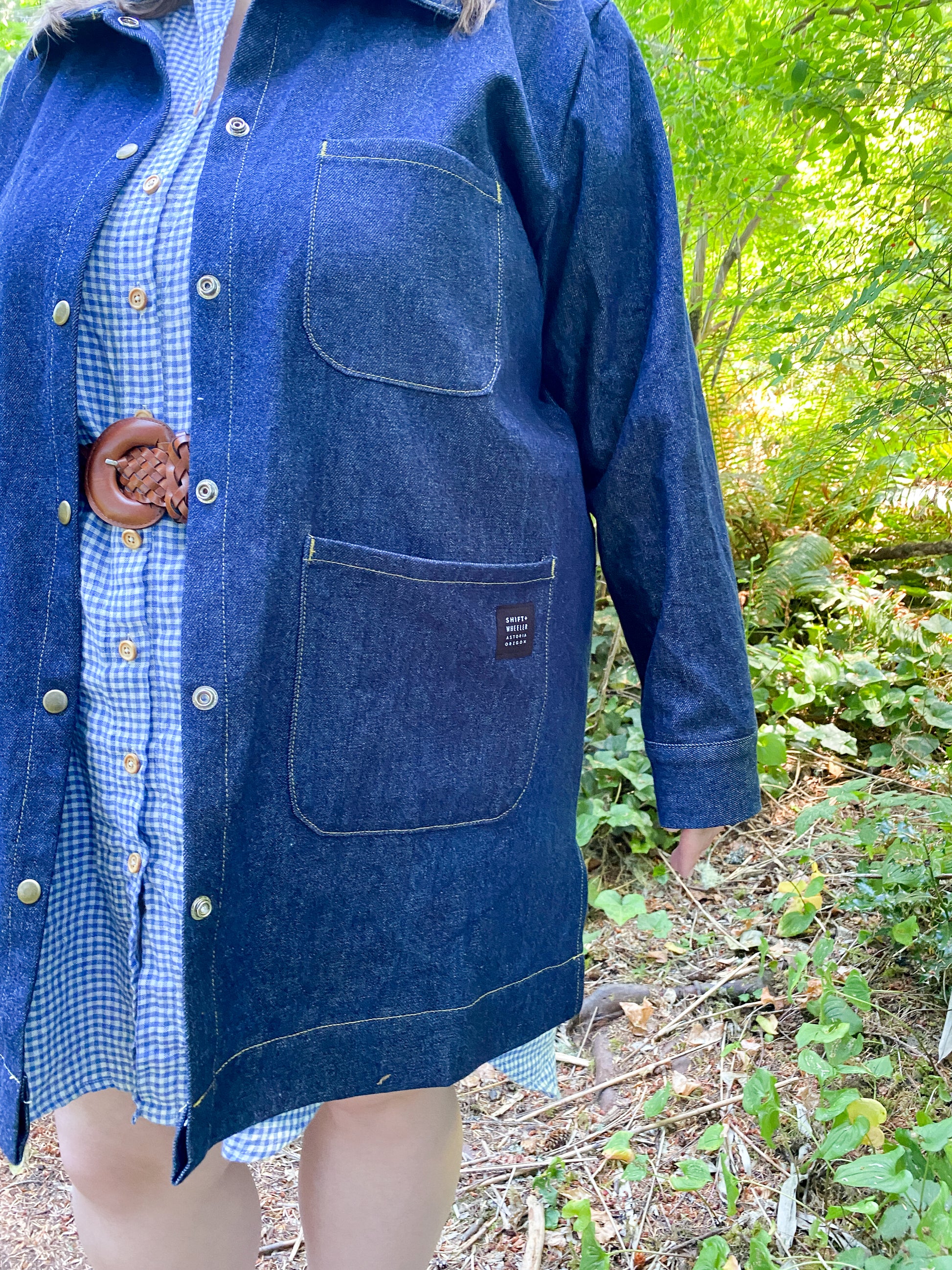 Close up detail of Denim Jacket that shows top stitching, large pockets, and snap buttons. 
