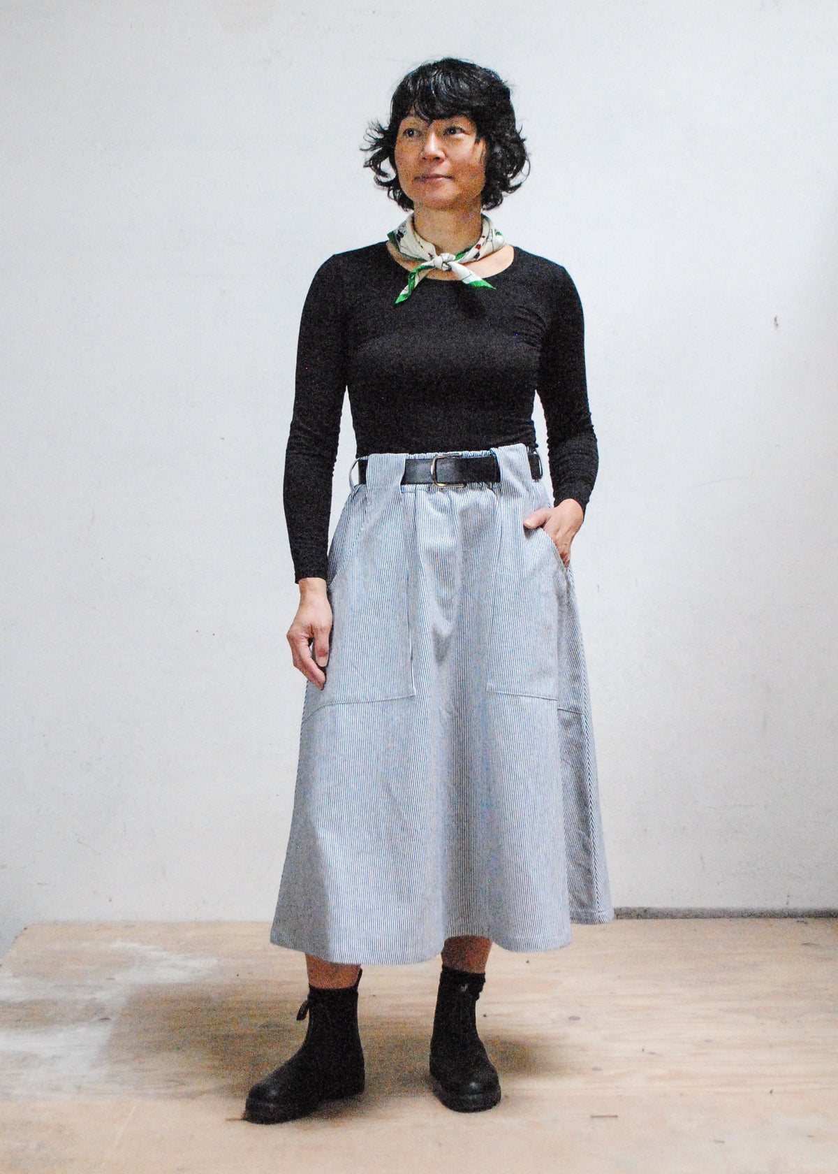 Model in long sleeve black shirt, black boots, and Shift + Wheeler handmade railroad stripe skirt, one hand in skirt pocket