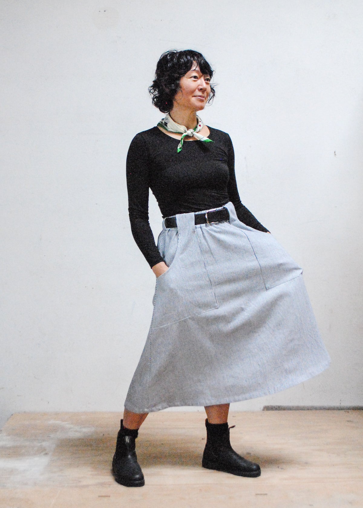 Model in black long sleeve shirt, black boots, and Shift + Wheeler handmade railroad stripe skirt, hands in skirt pockets