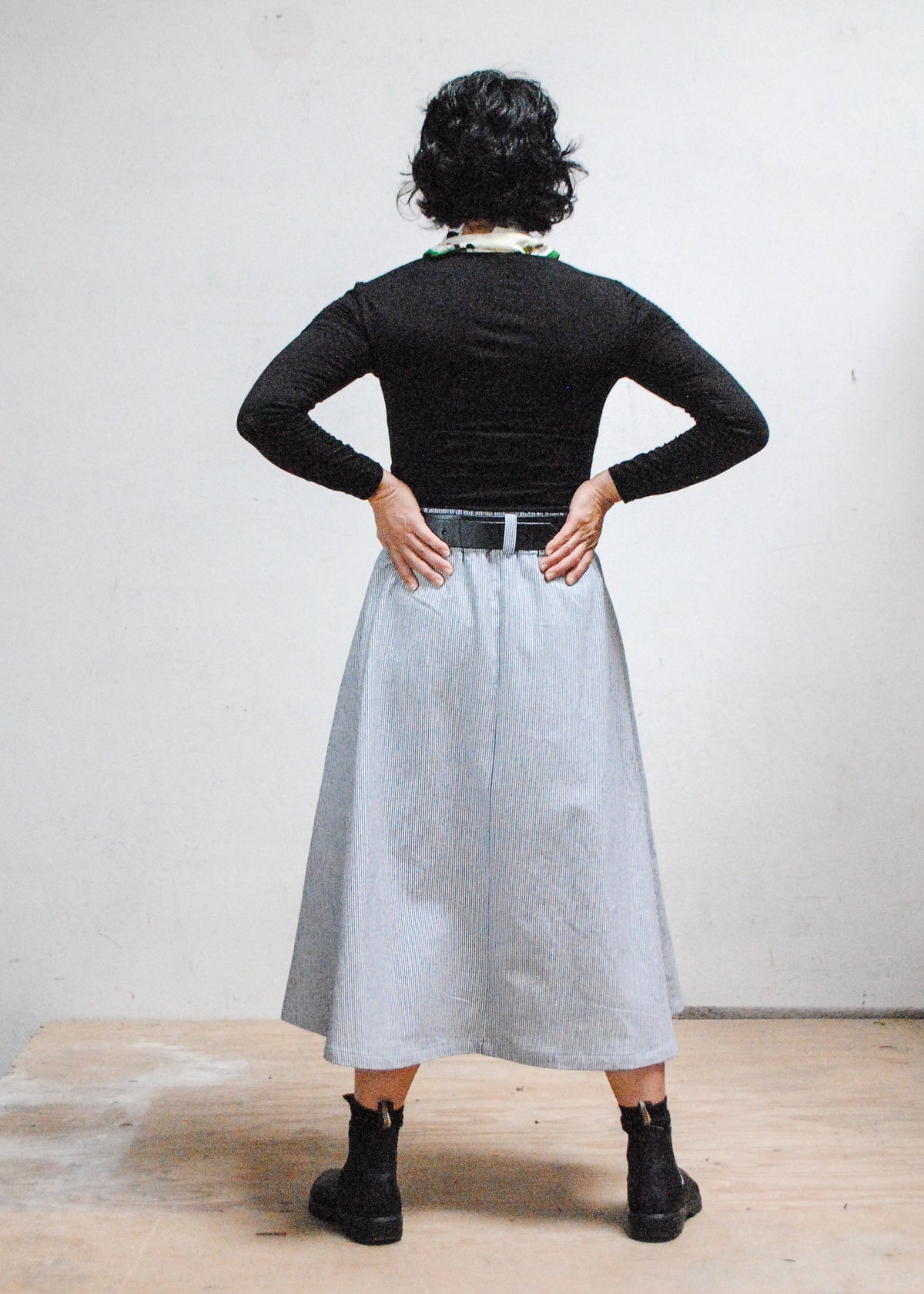 Model in black long sleeve shirt, black boots, and Shift + Wheeler handmade railroad stripe skirt - back view