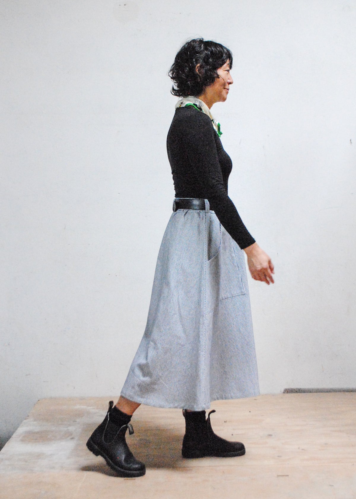 Model in black long sleeve shirt, black boots, and Shift + Wheeler handmade railroad stripe skirt - side view