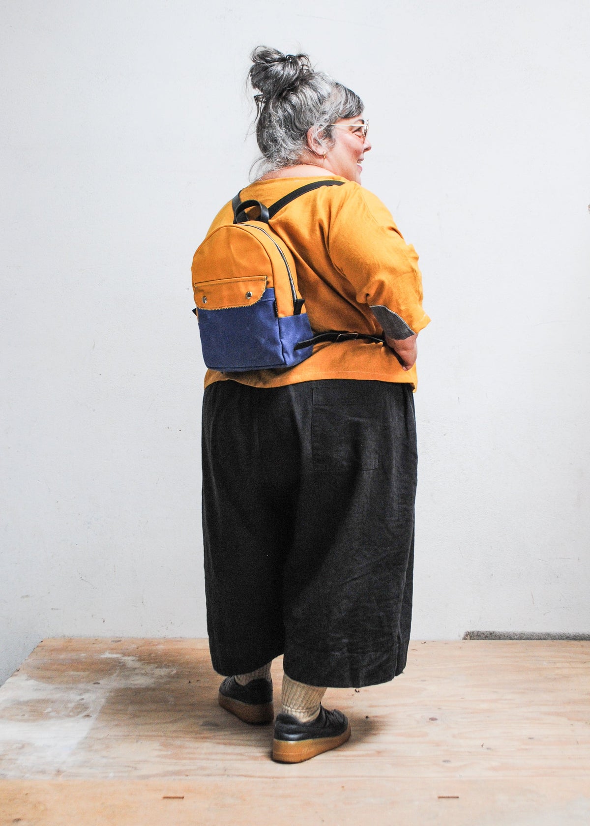 Model wearing 2-tone yellow gold and royal handmade Shift + Wheeler waxed canvas mini backpack - back view