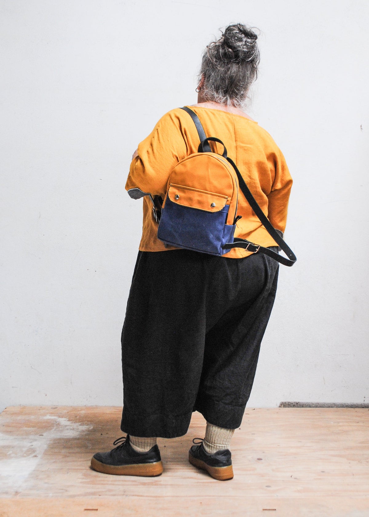 Model wearing 2-tone yellow gold and royal handmade Shift + Wheeler waxed canvas mini backpack on one shoulder - back view