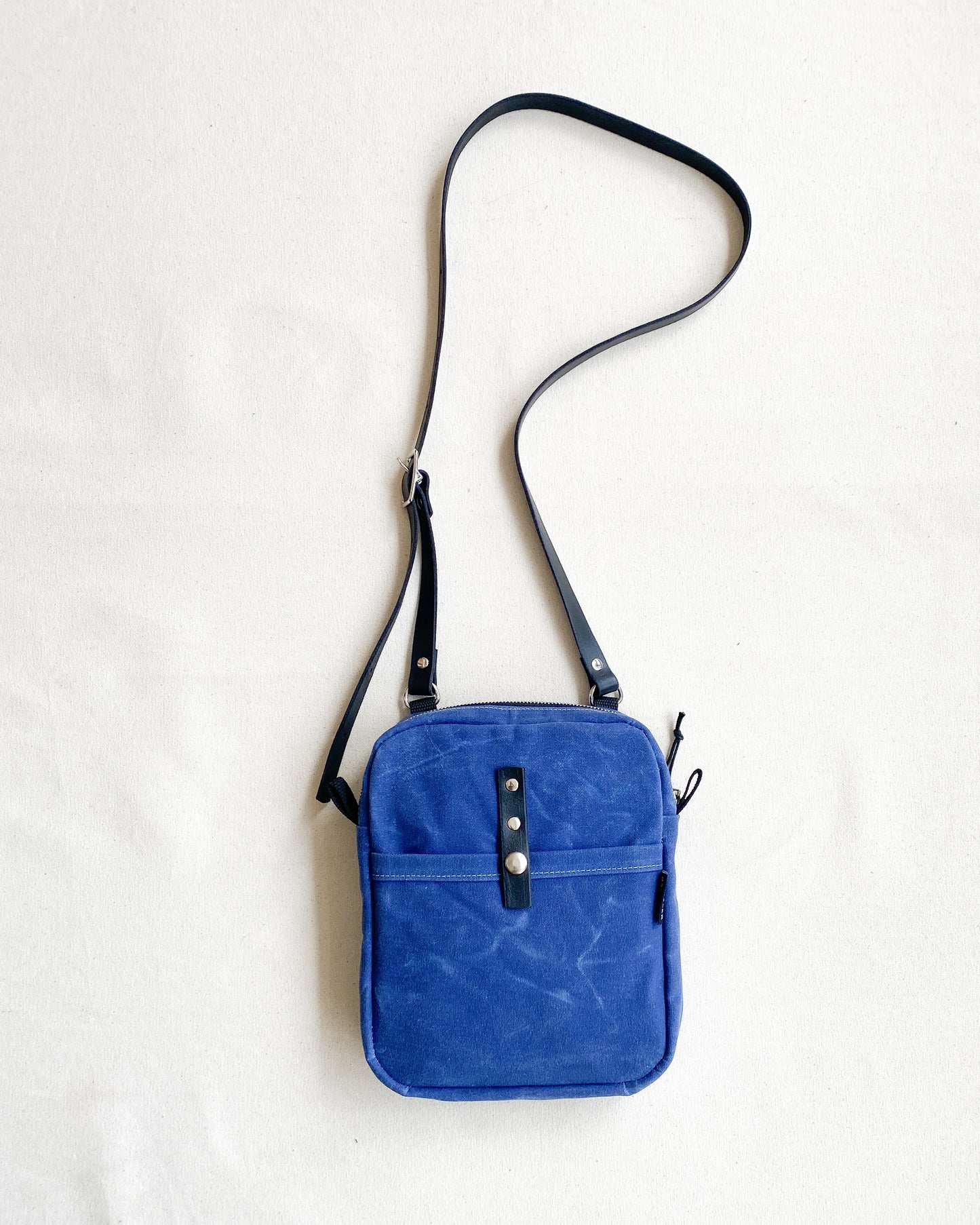 Handmade waxed canvas mini messenger bag with adjustable leather strap, front view