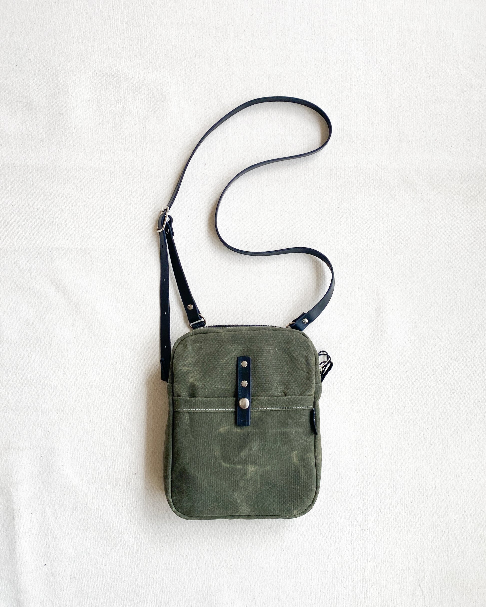 Waxed Canvas Mini Messenger bag in olive canvas with a black leather crossbody strap. 