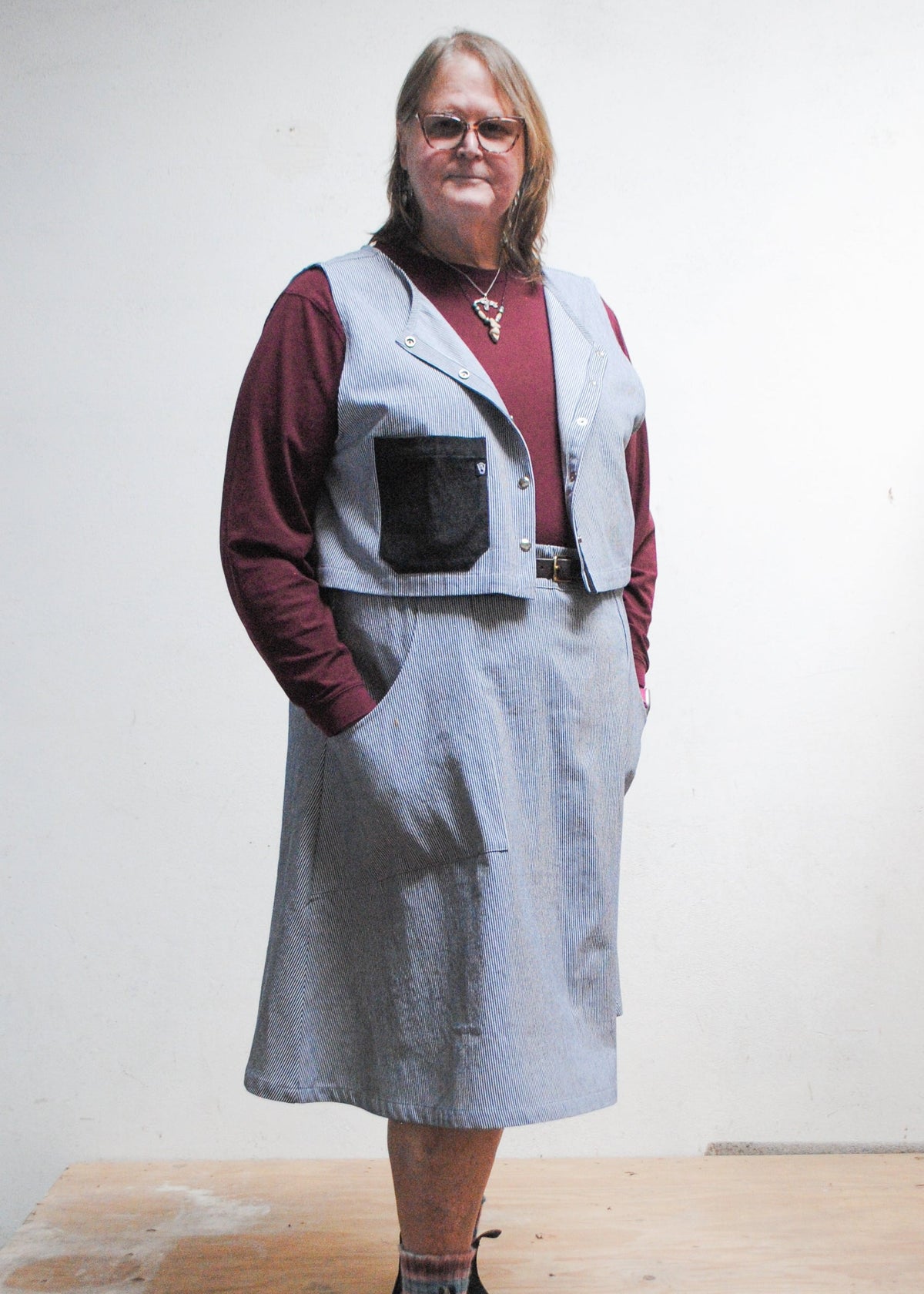 Model in burgundy longsleeve top, railroad strip vest, and Shift + Wheeler handmade railroad stripe skirt, hands in skirt pockets