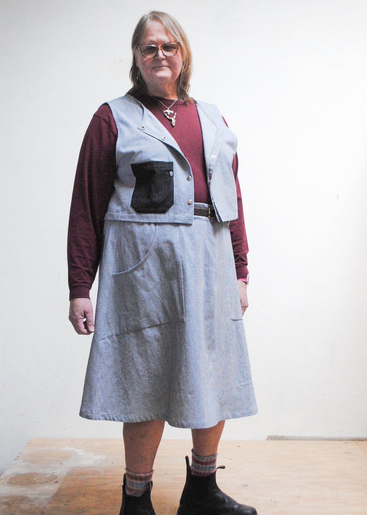 Model in burgundy long sleeve shirt, railroad strip vest, boots, and Shift + Wheeler handmade railroad stripe skirt
