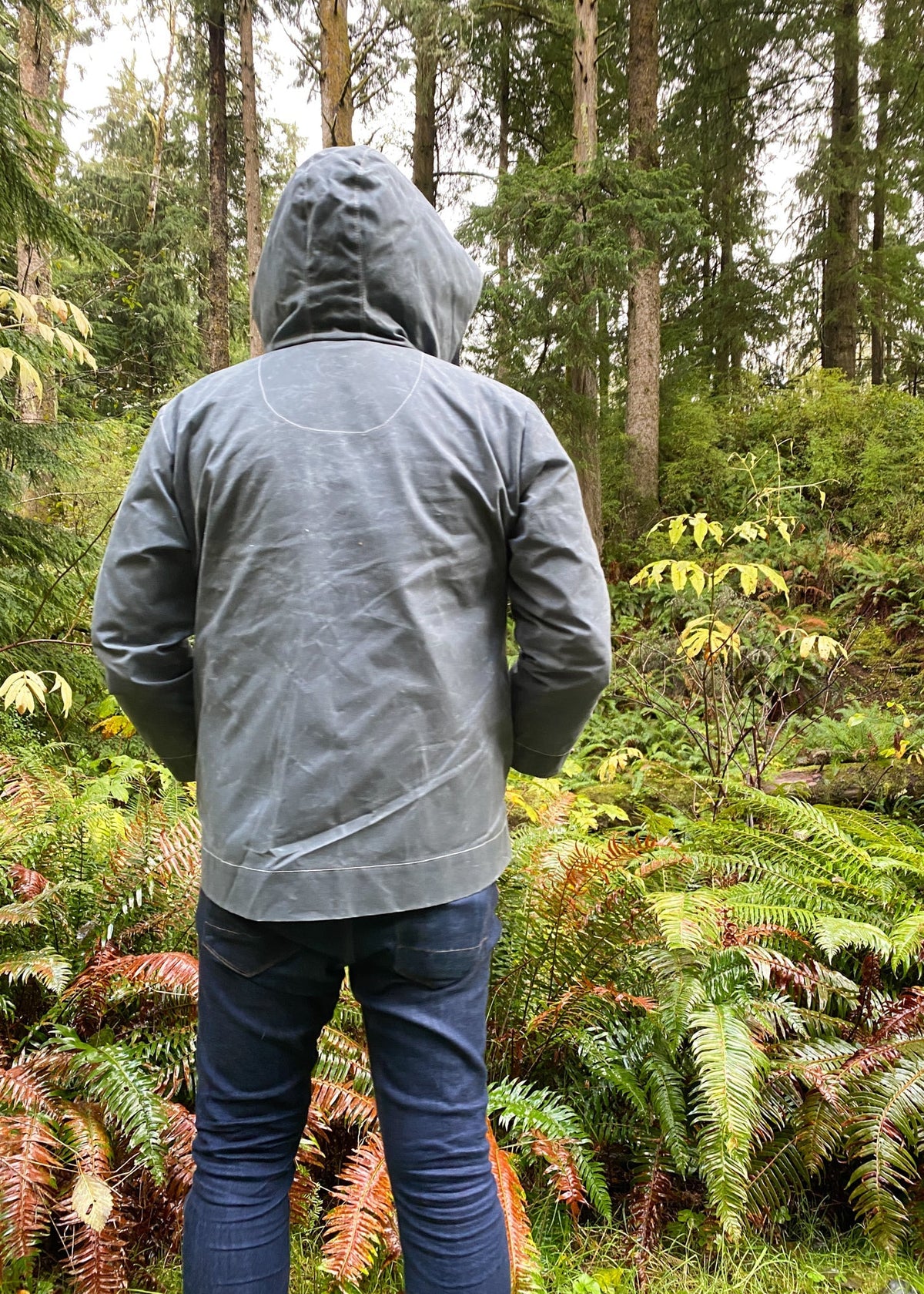 Model wearing Waxed Canvas Raincoat in Slate in forest setting. Back view