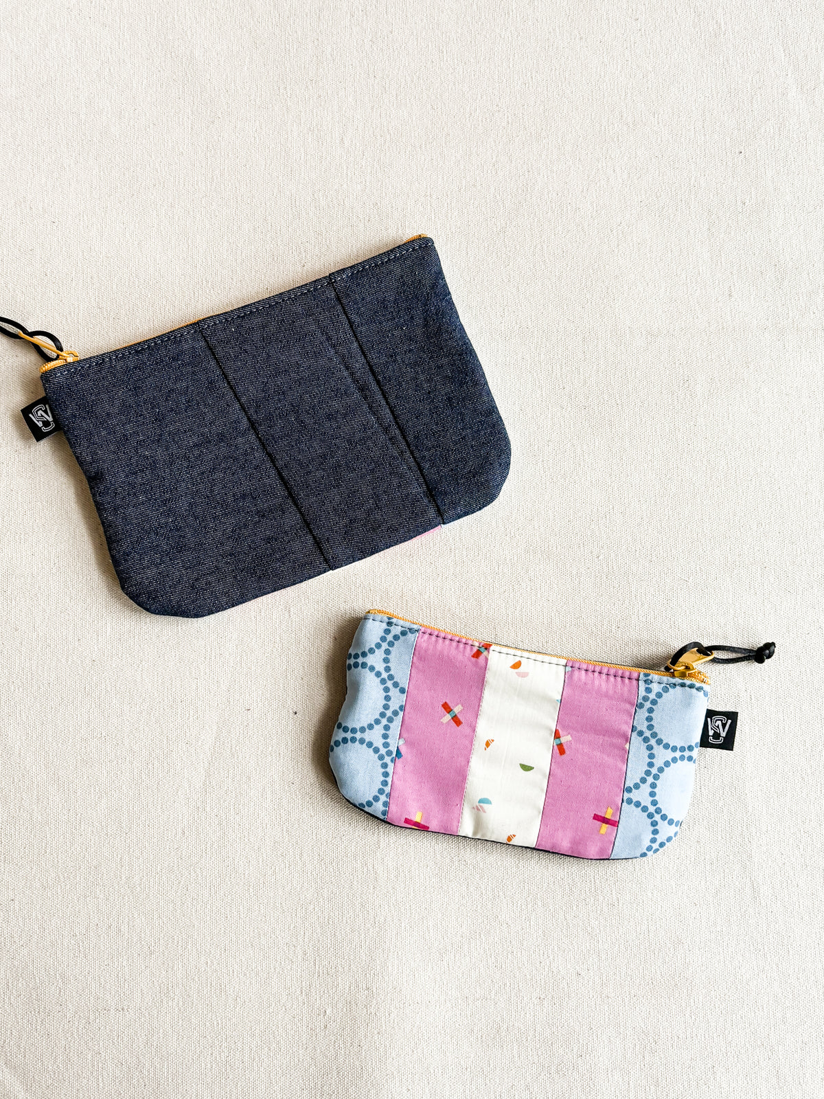 2 zipper pouches made out of scrap fabric, one in charcoal fabric and one with trans pride flag colors