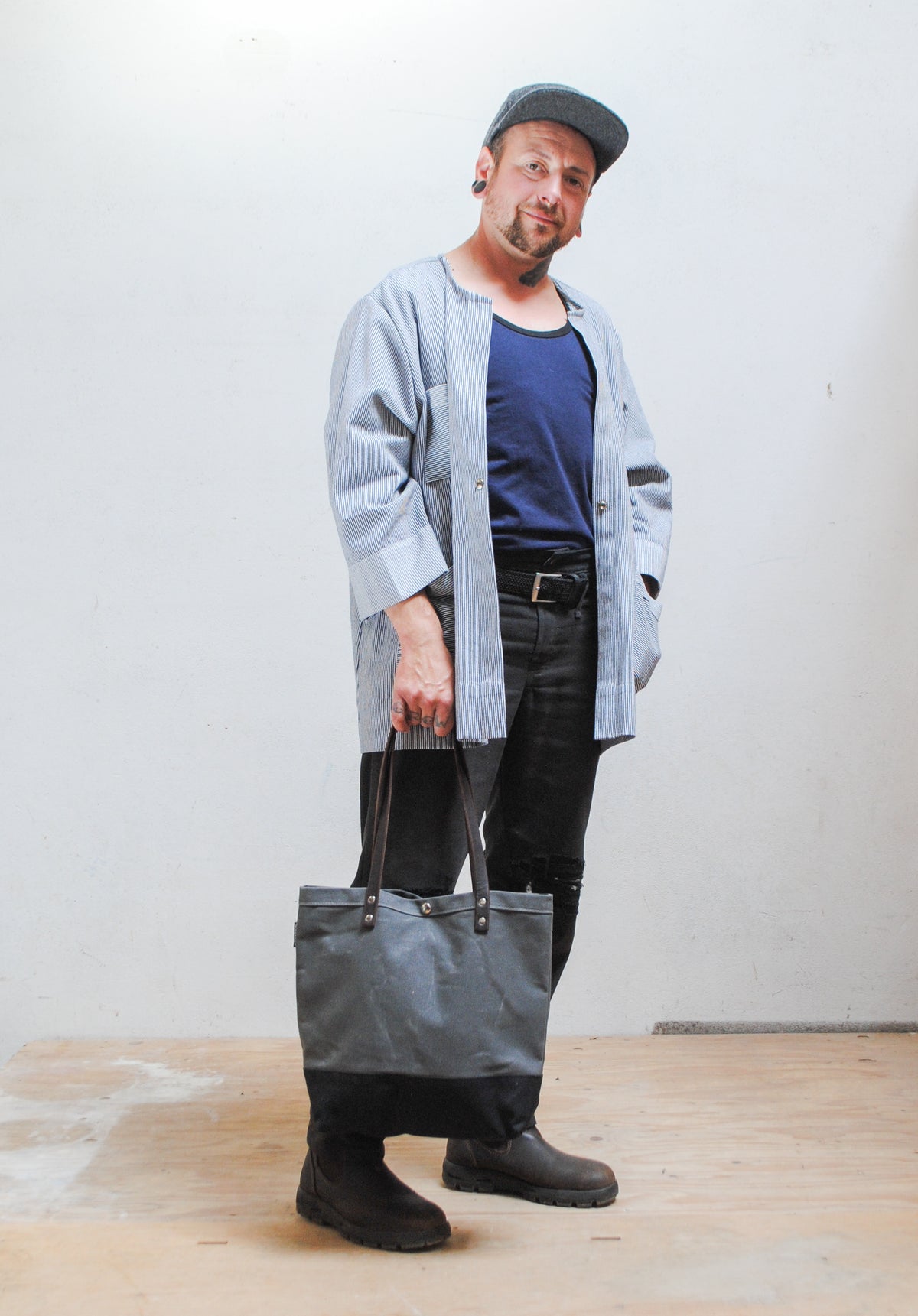 Queer person holding a gray tote bag against a plain background