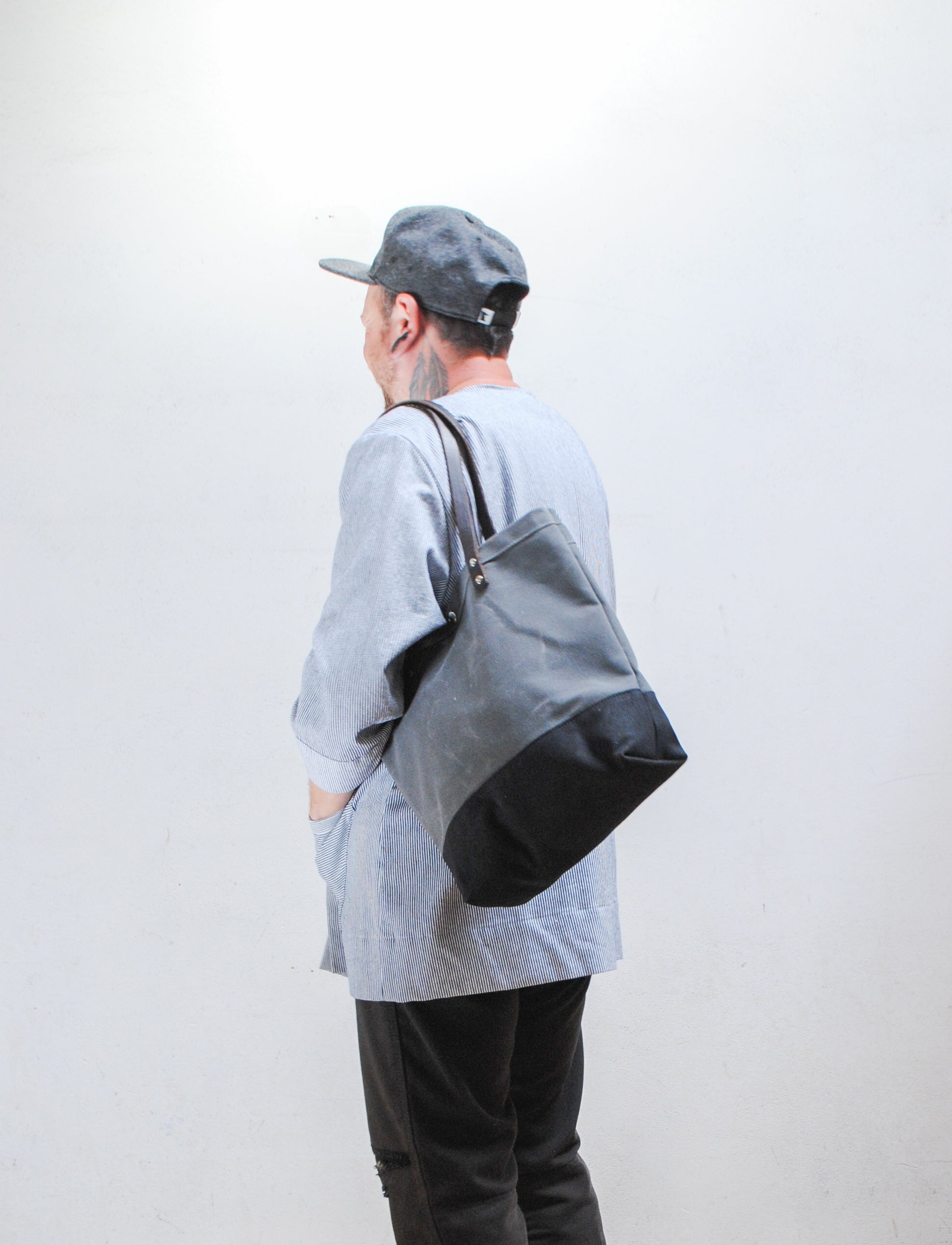 Person wearing a gray cap and holding a gray and black bag against a white background