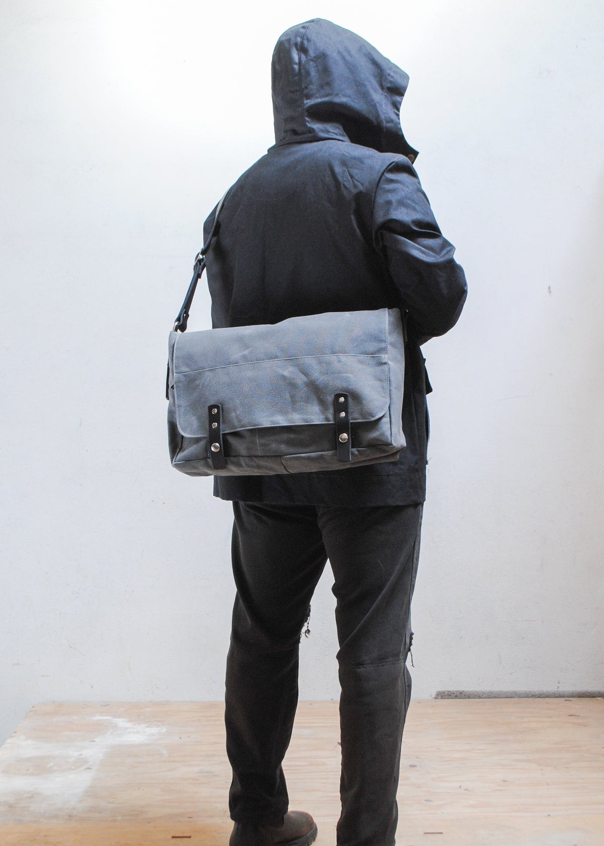 Model wearing black Shift + Wheeler black raincoat and charcoal Shift + Wheeler waxed canvas messenger bag over the back of shoulder