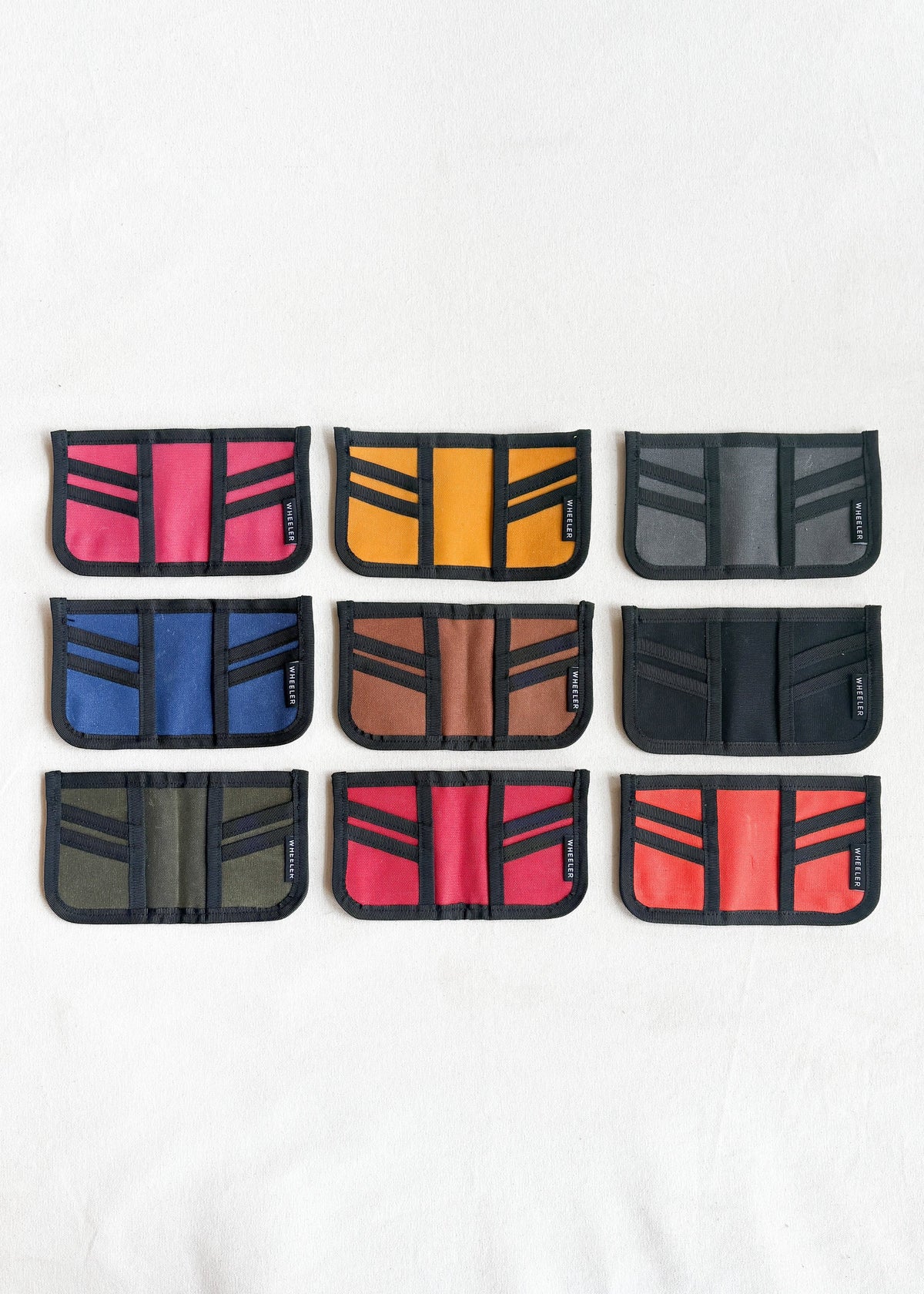Group shot of nine Shift + Wheeler waxed canvas wallets laid flat in variety of color options