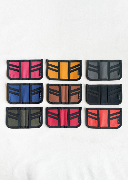 Group shot of nine Shift + Wheeler waxed canvas wallets laid flat in variety of color options