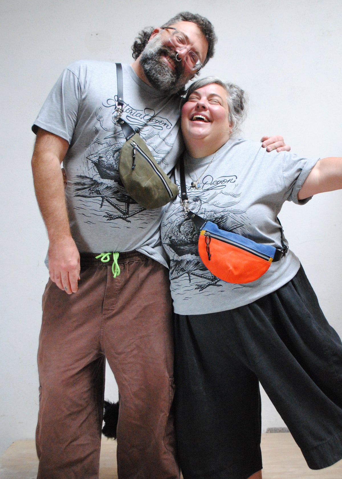 Two joyful pals joining in a side hug while wearing handmade waxed canvas fanny packs