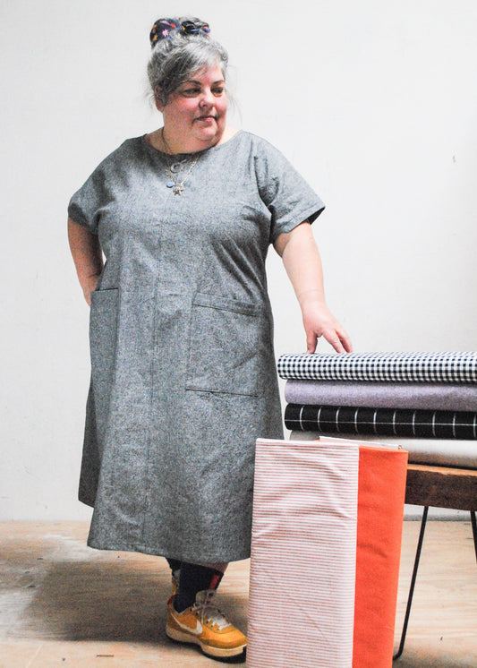 Woman in grey made-to-order dress standing with hand on stack of fabric options