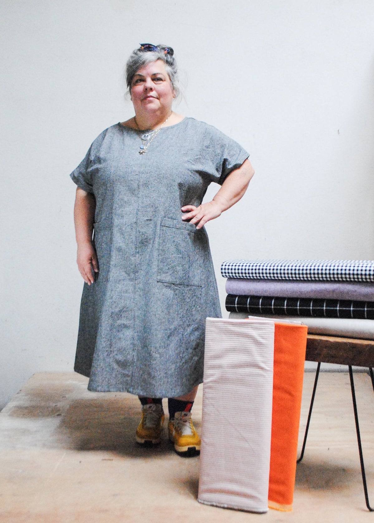 Woman in grey made-to-order dress standing with hand on hip next to stack of fabric options