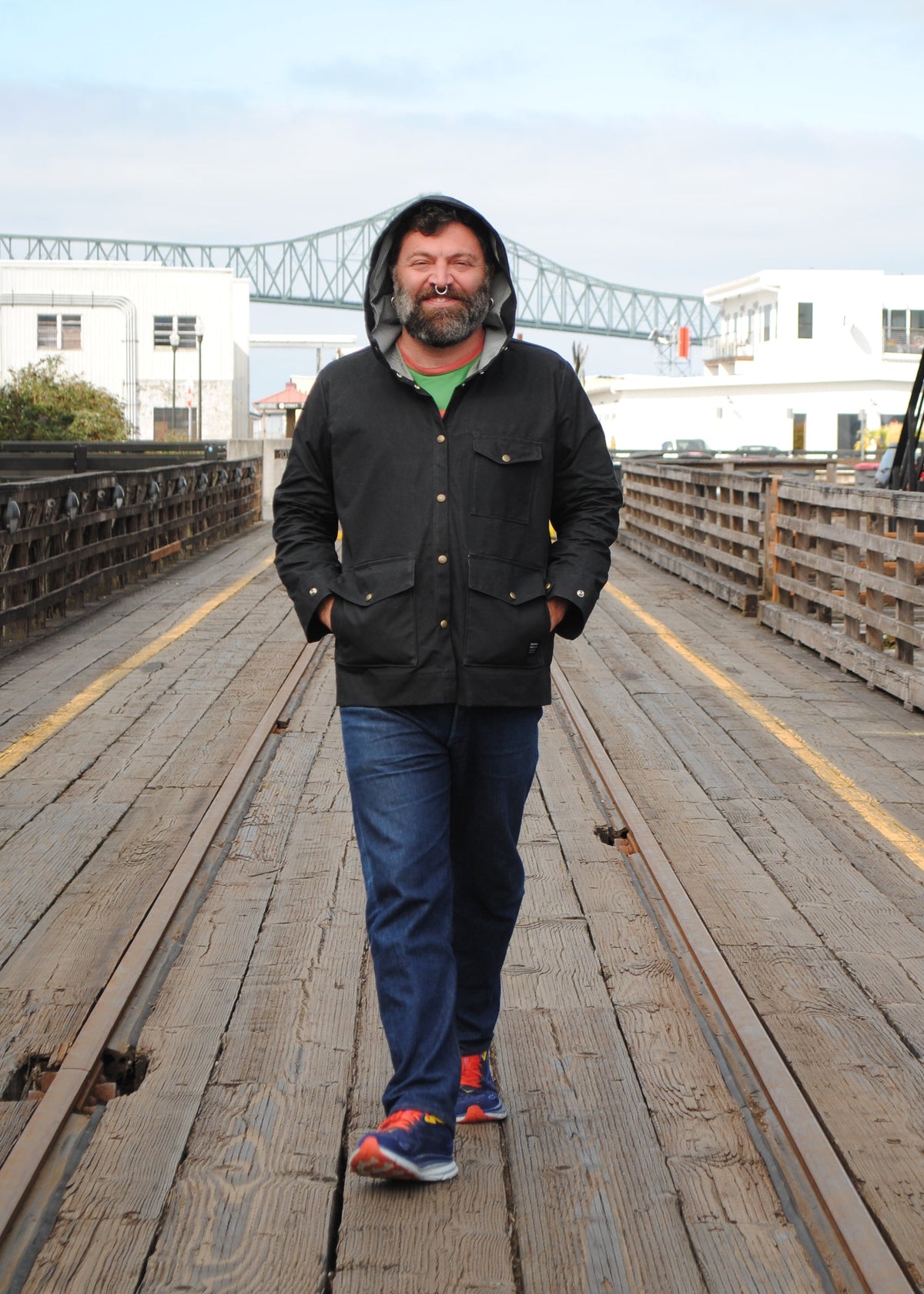 Front view of model wearing black waxed canvas rain jacket while walking with hands in waist pockets of jacket
