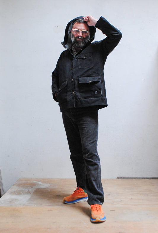 Model wearing black waxed canvas rain jacket with hood up