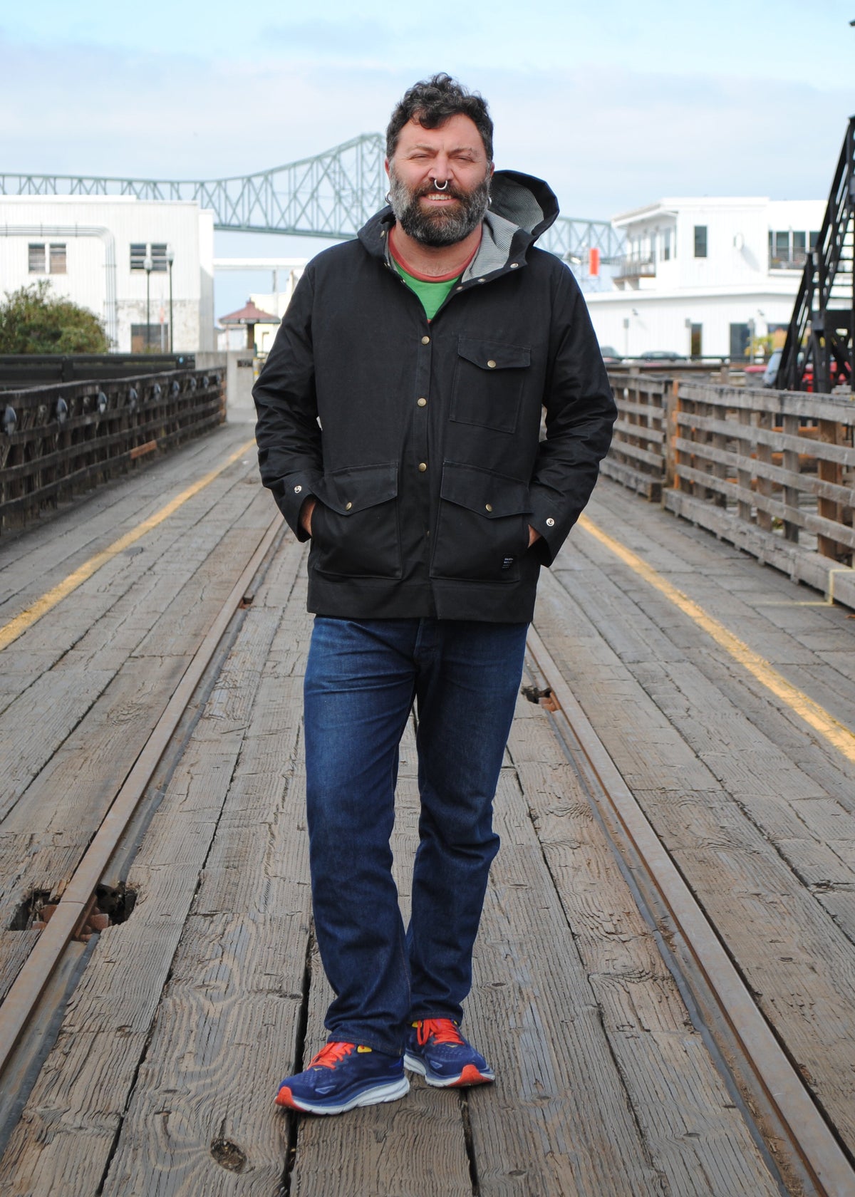 Model wearing black waxed canvas rain jacket with hands tucked into waist pockets in an outdoor setting
