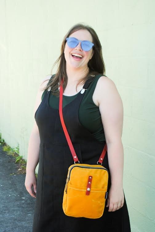 3/4 angle of model wearing black linen suspender dress. Also wearing Wheeler Bag Co. yellow mini messenger bag.