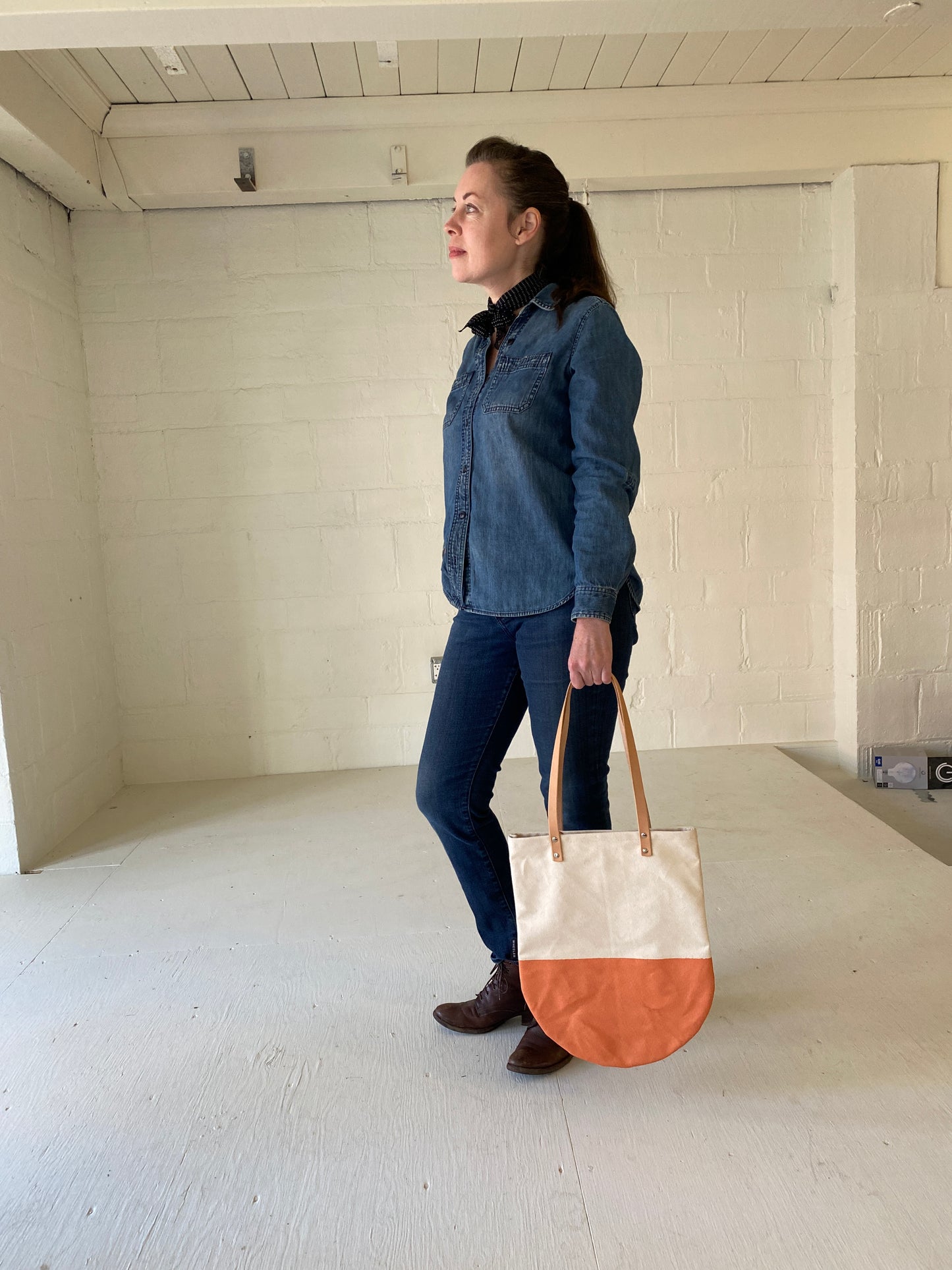 Unwaxed Natural canvas round bottom tote with orange rubber painted bottom, on model. 