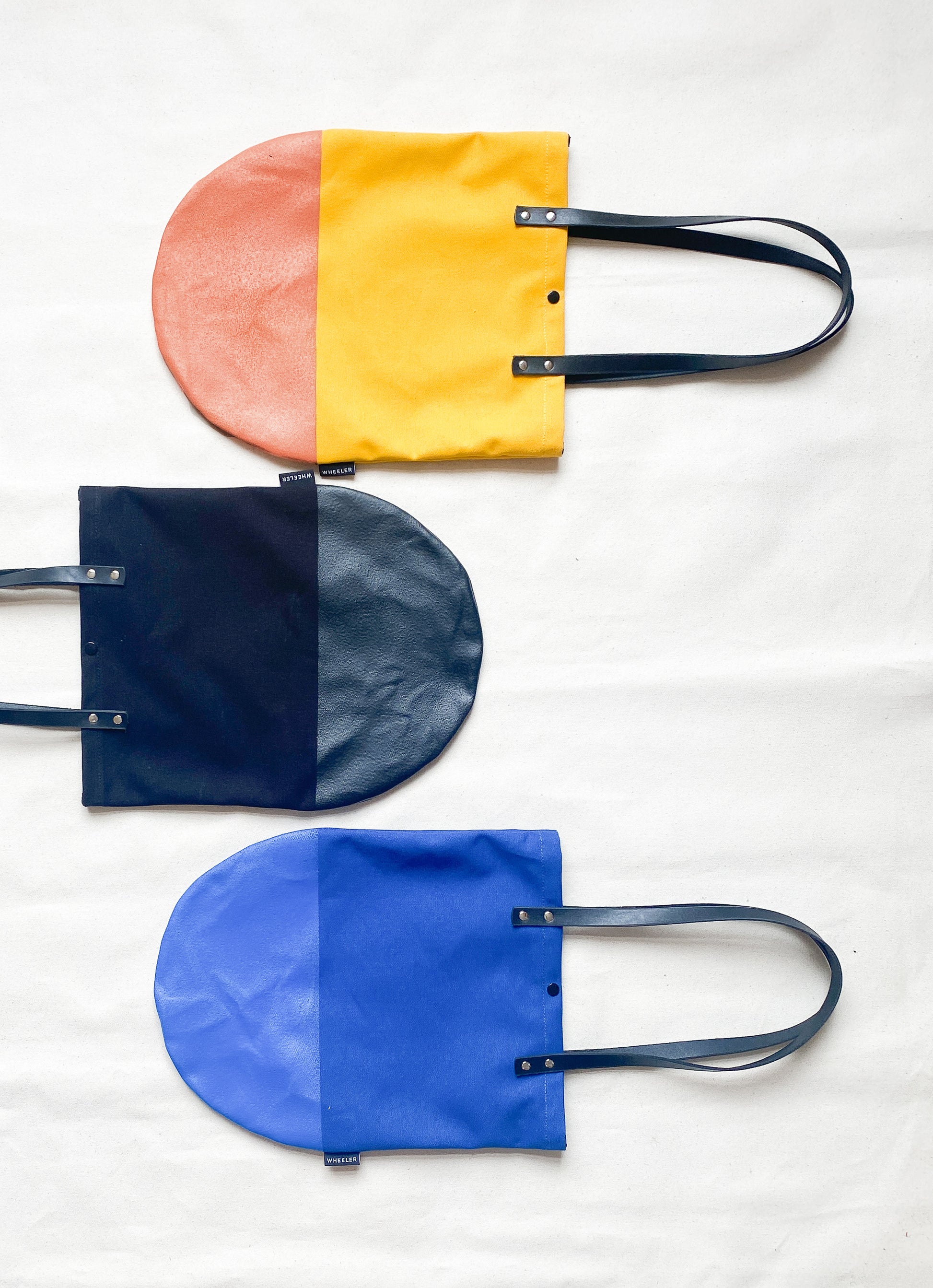 Round bottom totes in yellow, black, and blue. 
