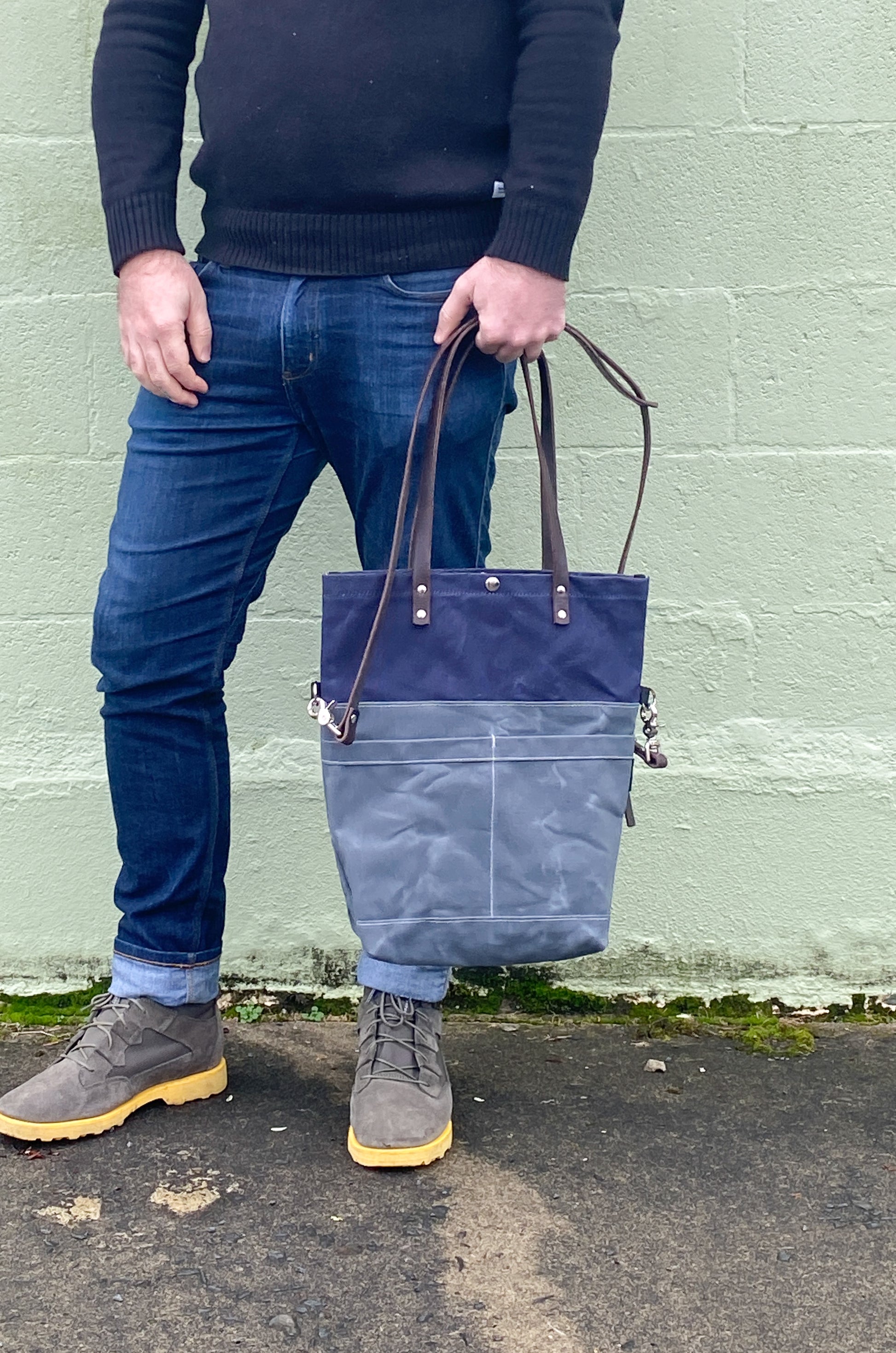 Model holding convertible tote with smaller handles in slate and navy. 