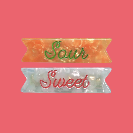 "Sour, Sweet" hair clip set. "Sour" clip in mandarin pearlescent acetate with bold green ink engraving. "Sweet" minty pearlescent acetate with pink engraved ink. 