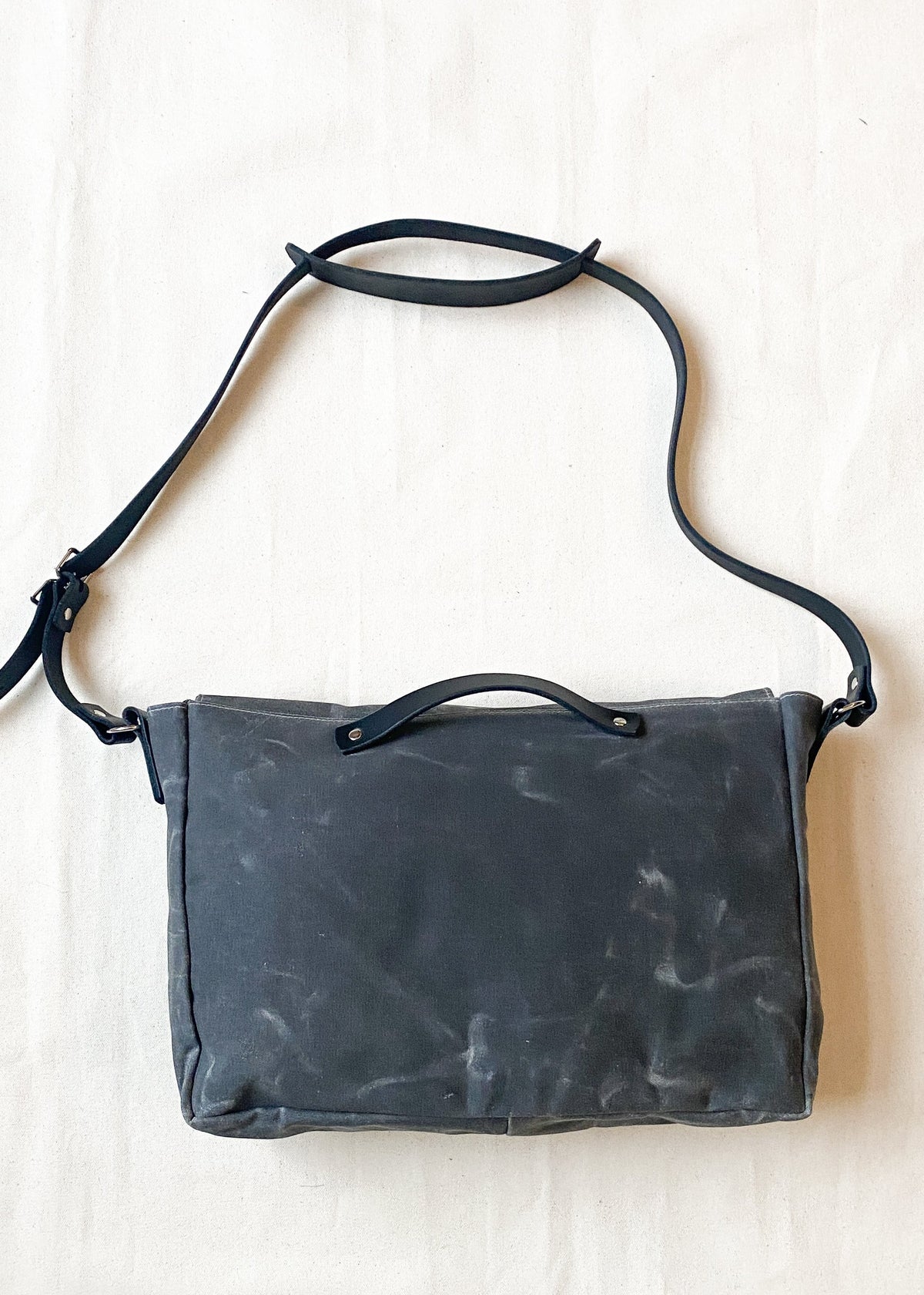 Charcoal waxed canvas messenger bag with black leather straps, back view